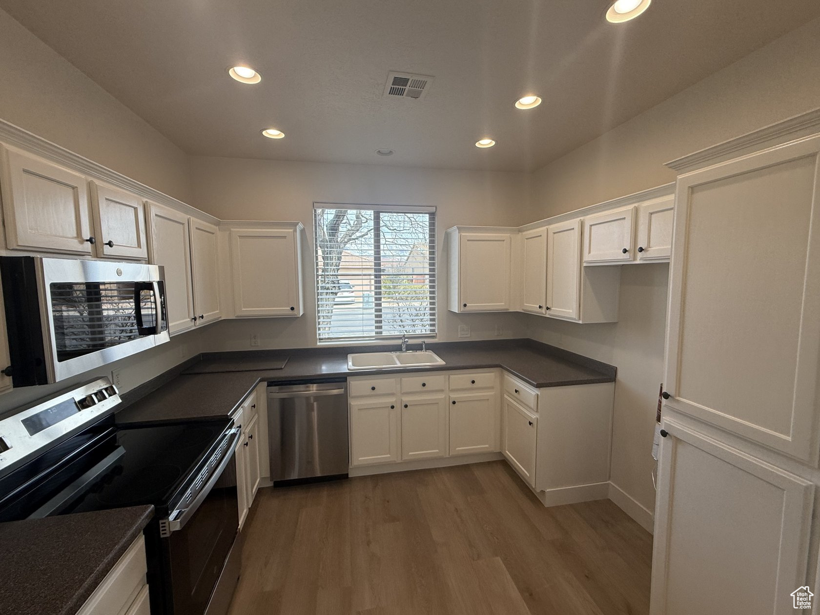 Kitchen with visible vents, a sink, white cabinets, appliances with stainless steel finishes, and dark countertops