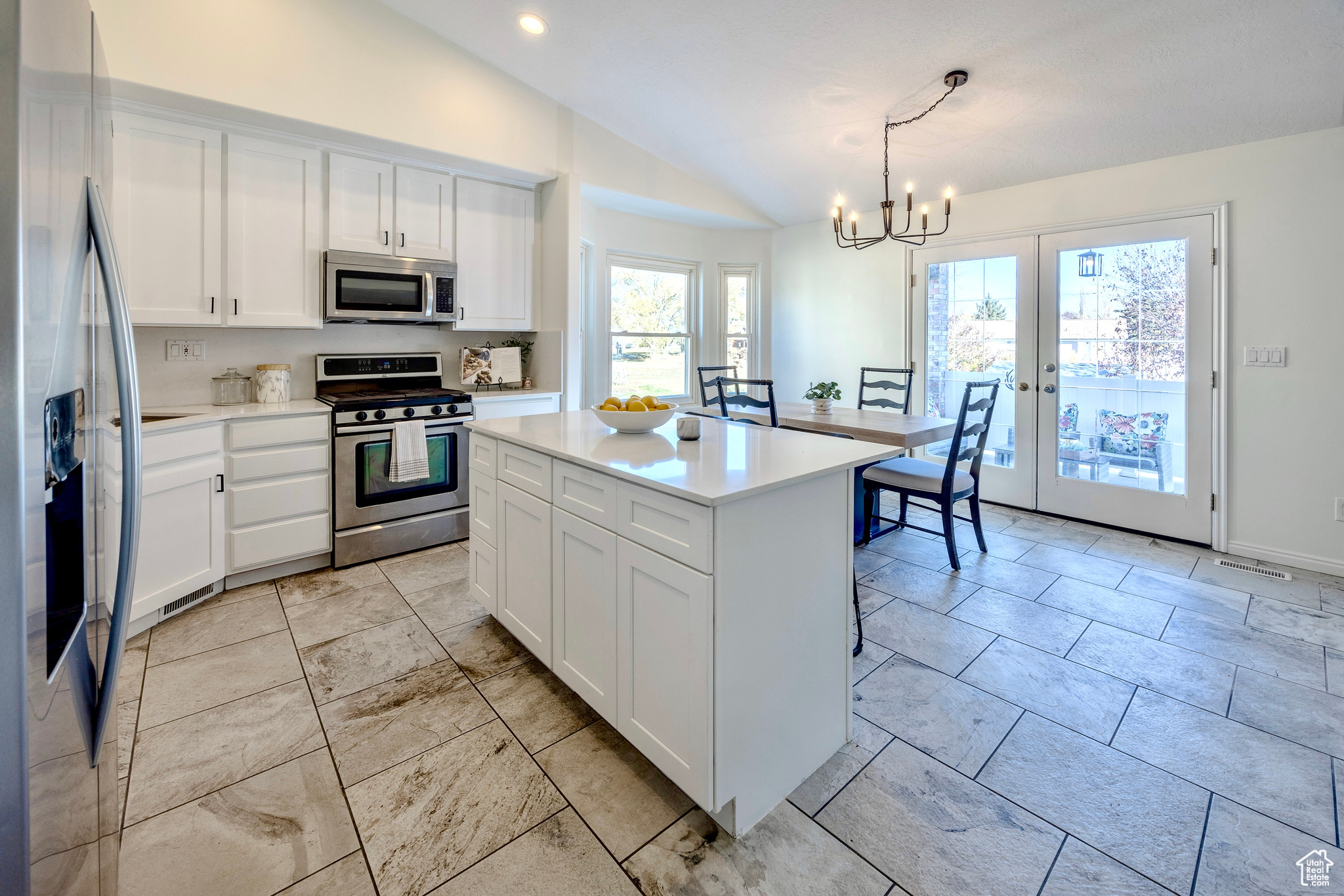 Kitchen with stainless steel appliances, lofted ceiling, light countertops, an inviting chandelier, and white cabinetry