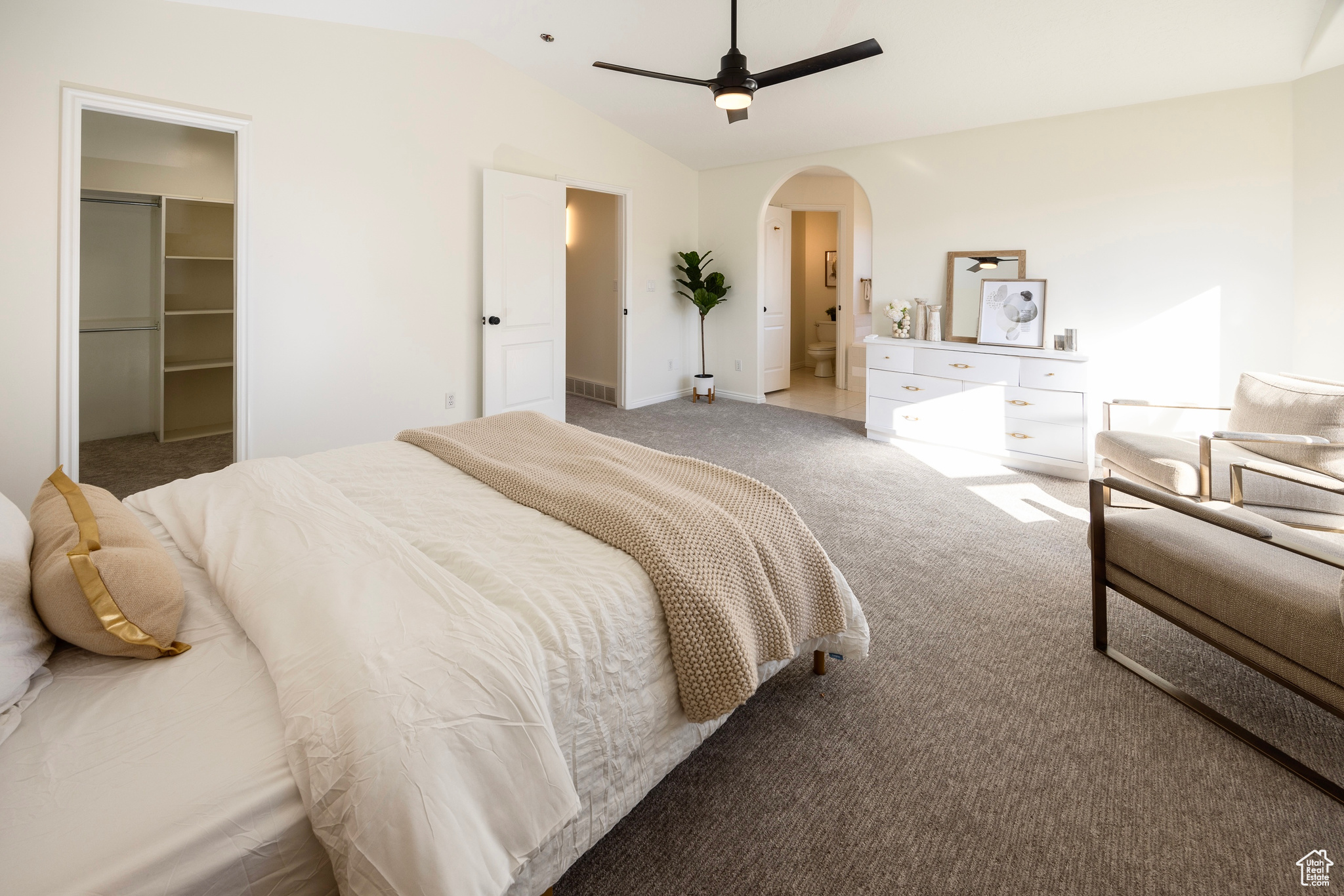 Bedroom with light carpet, arched walkways, connected bathroom, vaulted ceiling, and a walk in closet