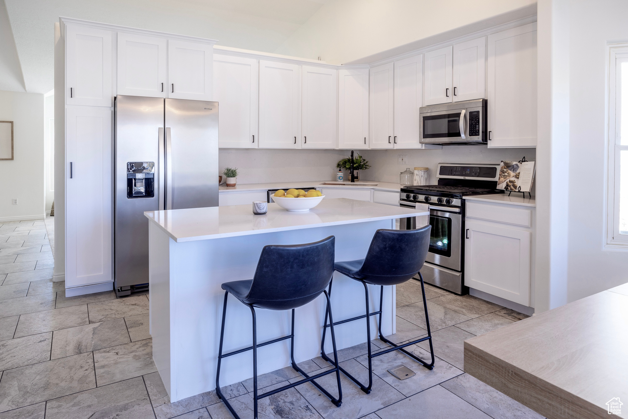 Kitchen with appliances with stainless steel finishes, a kitchen bar, white cabinetry, and a center island