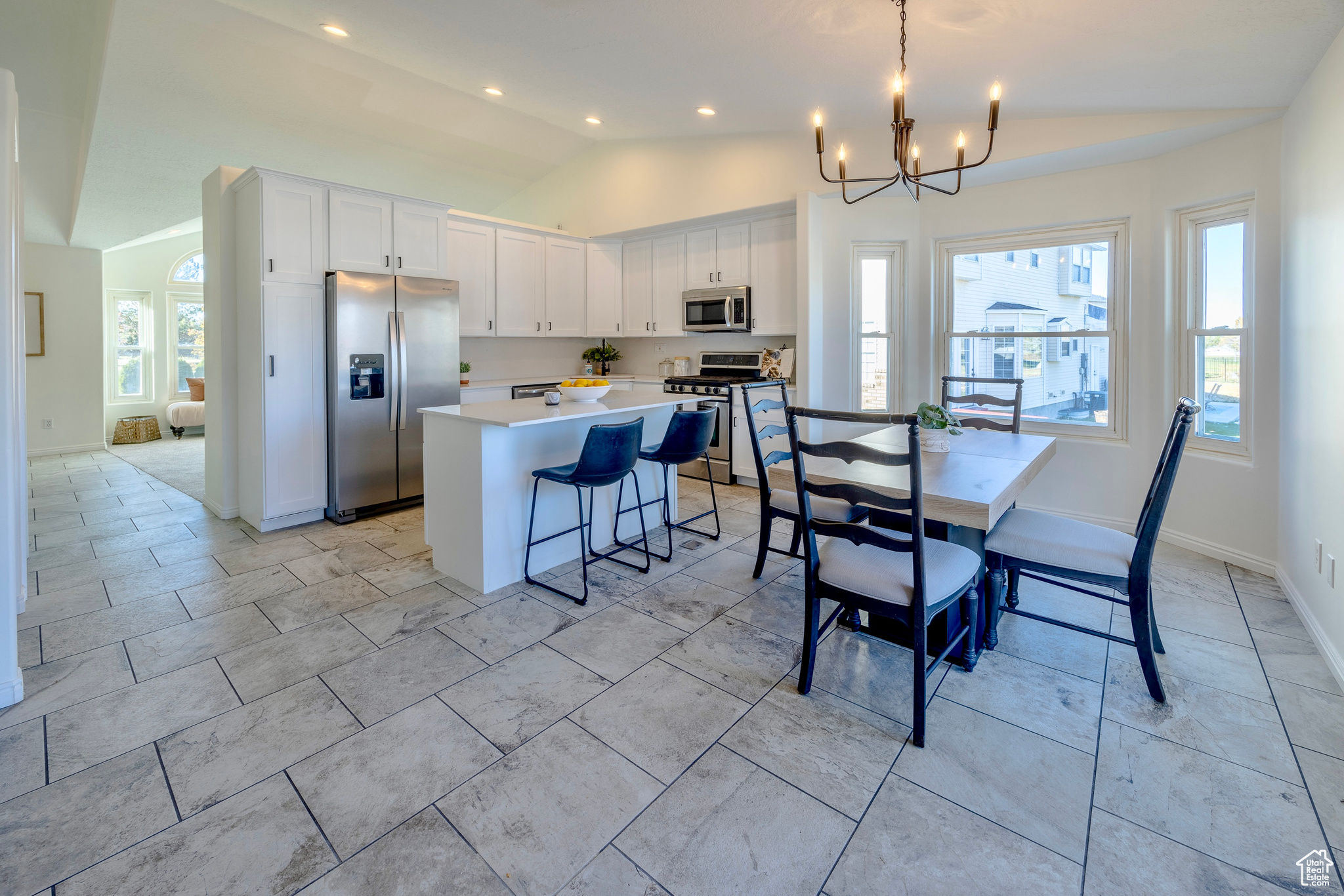 Kitchen with a breakfast bar, white cabinets, vaulted ceiling, appliances with stainless steel finishes, and a center island