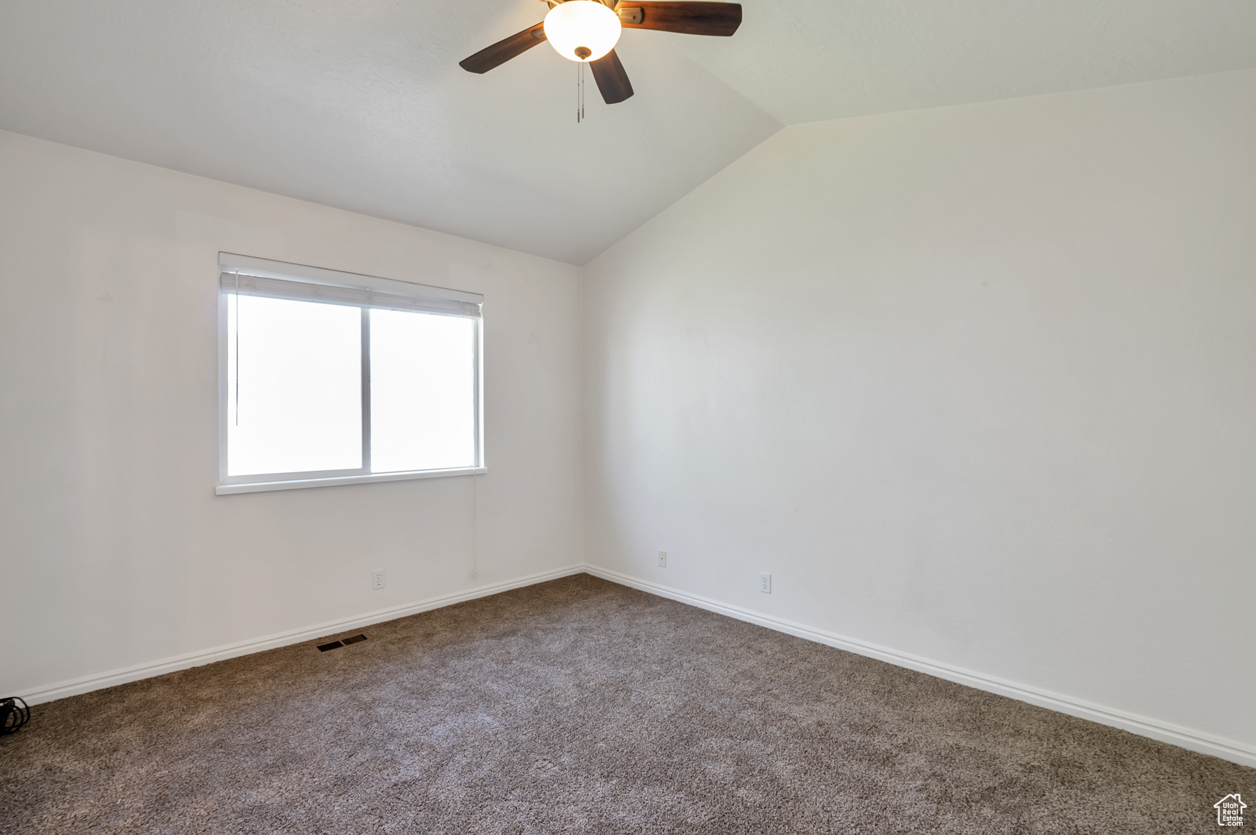 Carpeted empty room with vaulted ceiling, a ceiling fan, visible vents, and baseboards