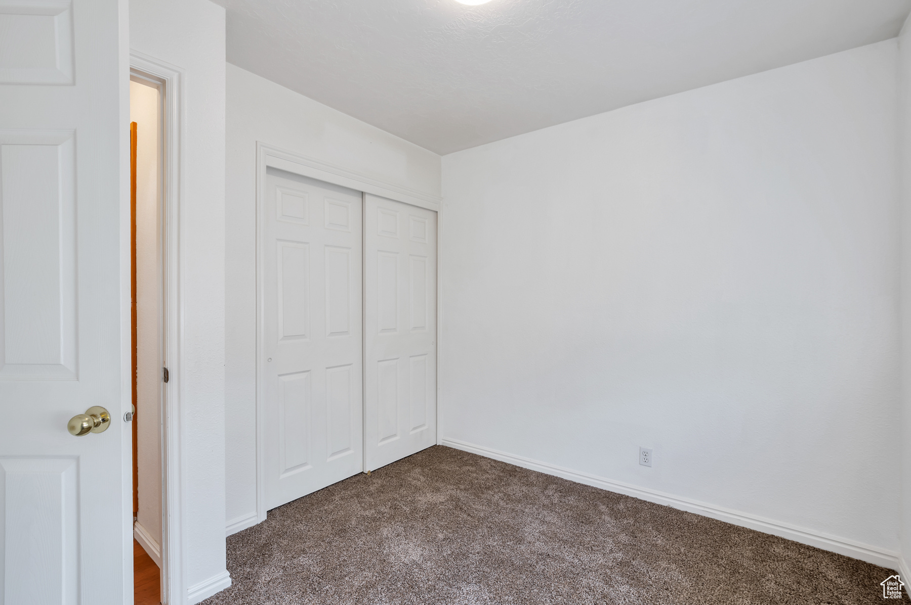 Unfurnished bedroom featuring dark colored carpet, a closet, and baseboards