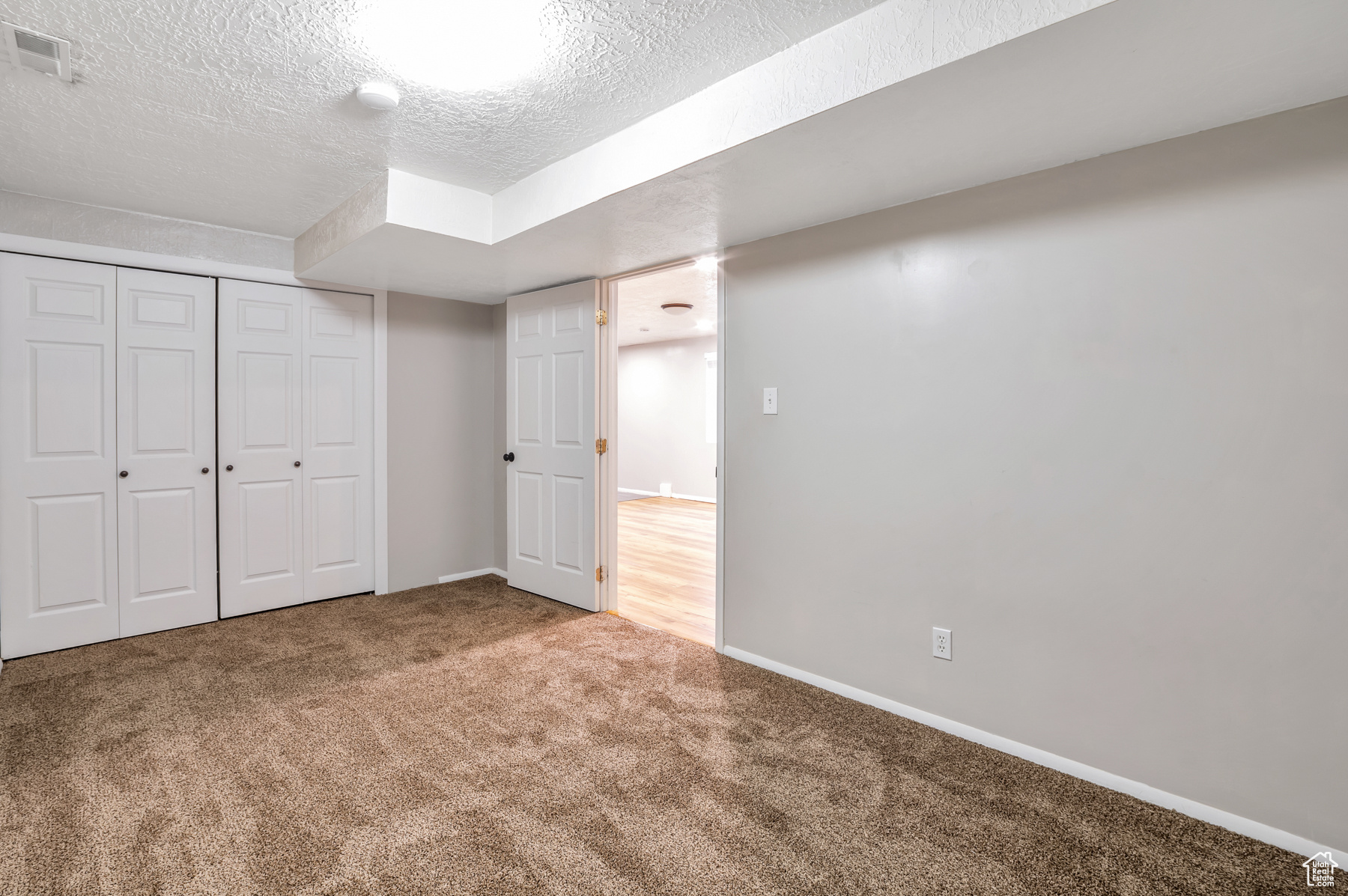 Below grade area featuring baseboards, visible vents, a textured ceiling, and carpet