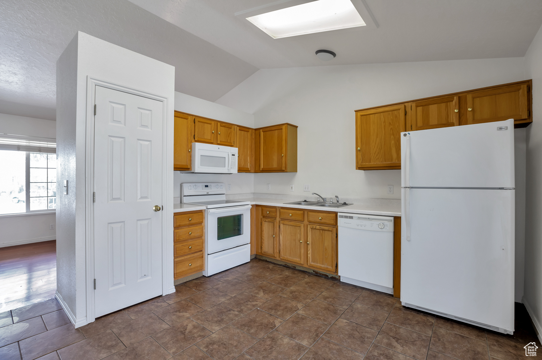 Kitchen with white appliances, baseboards, lofted ceiling, a sink, and light countertops