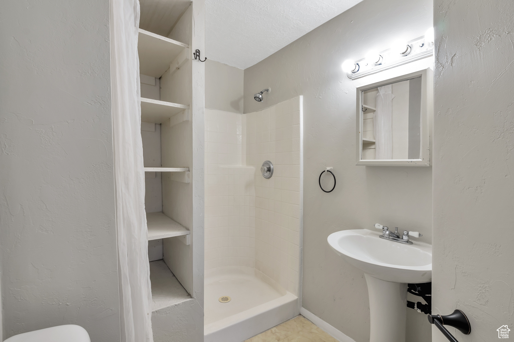 Full bathroom featuring a stall shower, toilet, and a textured wall