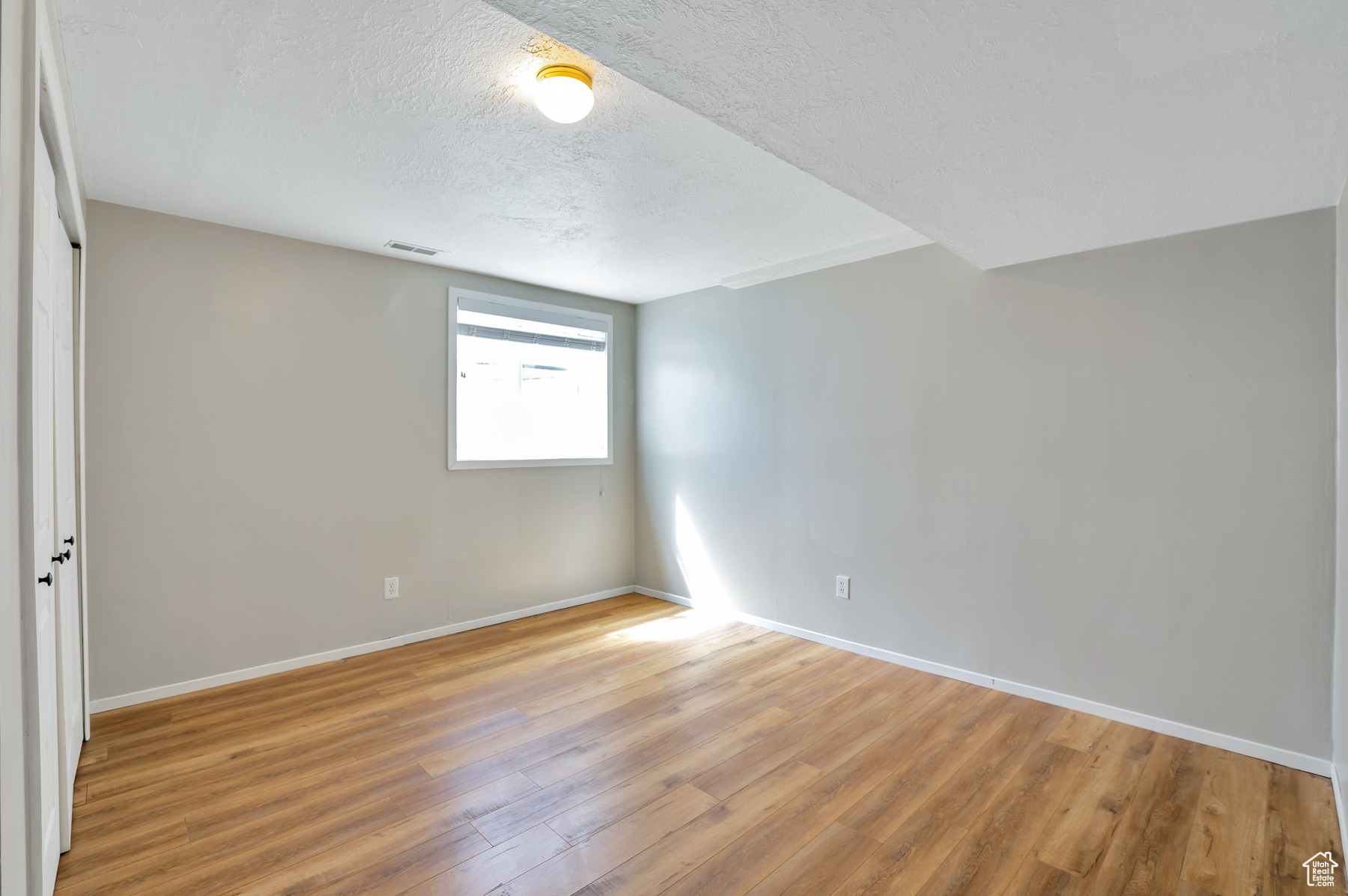 Empty room with visible vents, light wood-style flooring, a textured ceiling, and baseboards