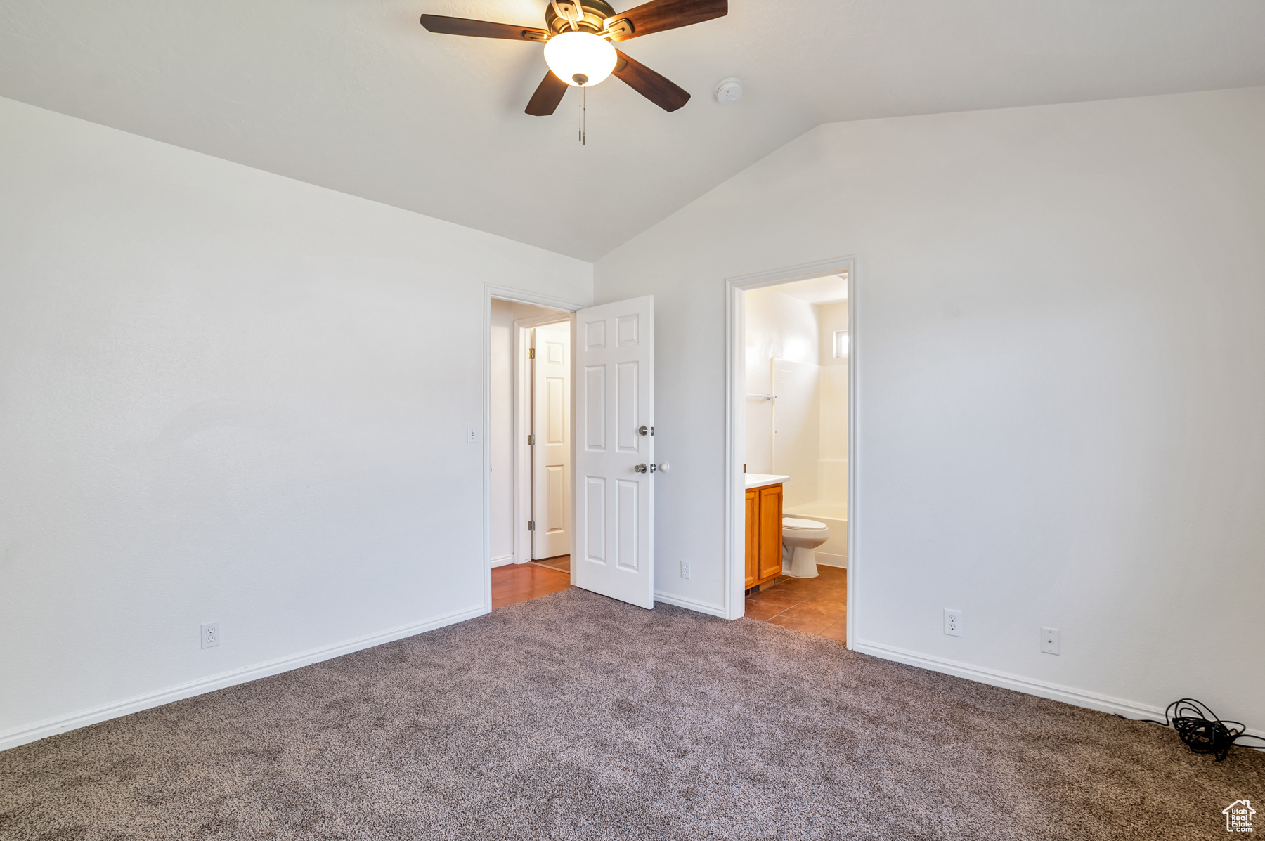 Unfurnished bedroom with connected bathroom, baseboards, carpet, ceiling fan, and lofted ceiling