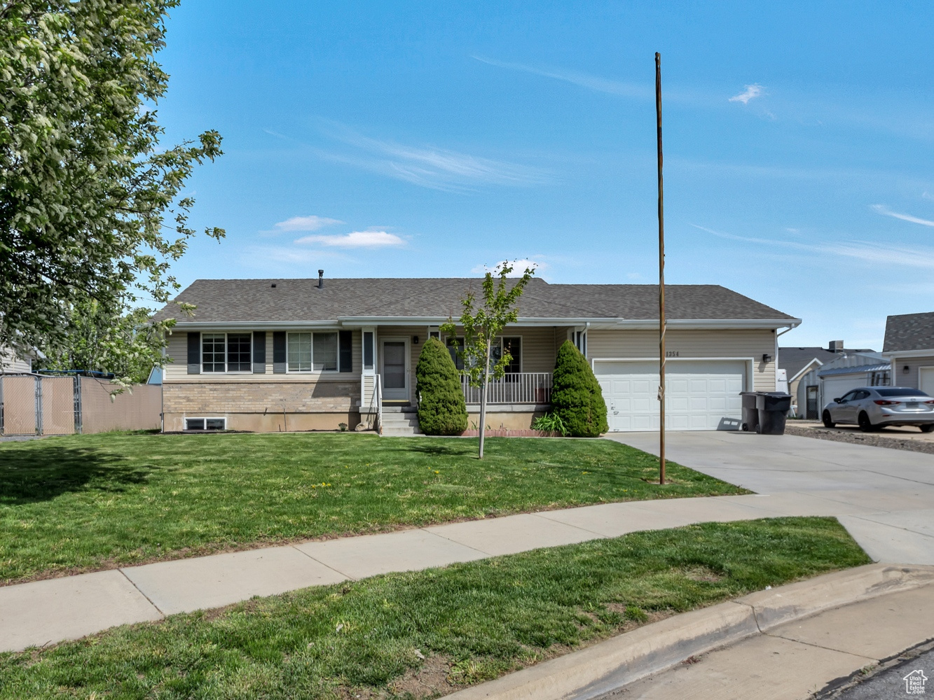 Ranch-style house with a front lawn, fence, covered porch, concrete driveway, and an attached garage