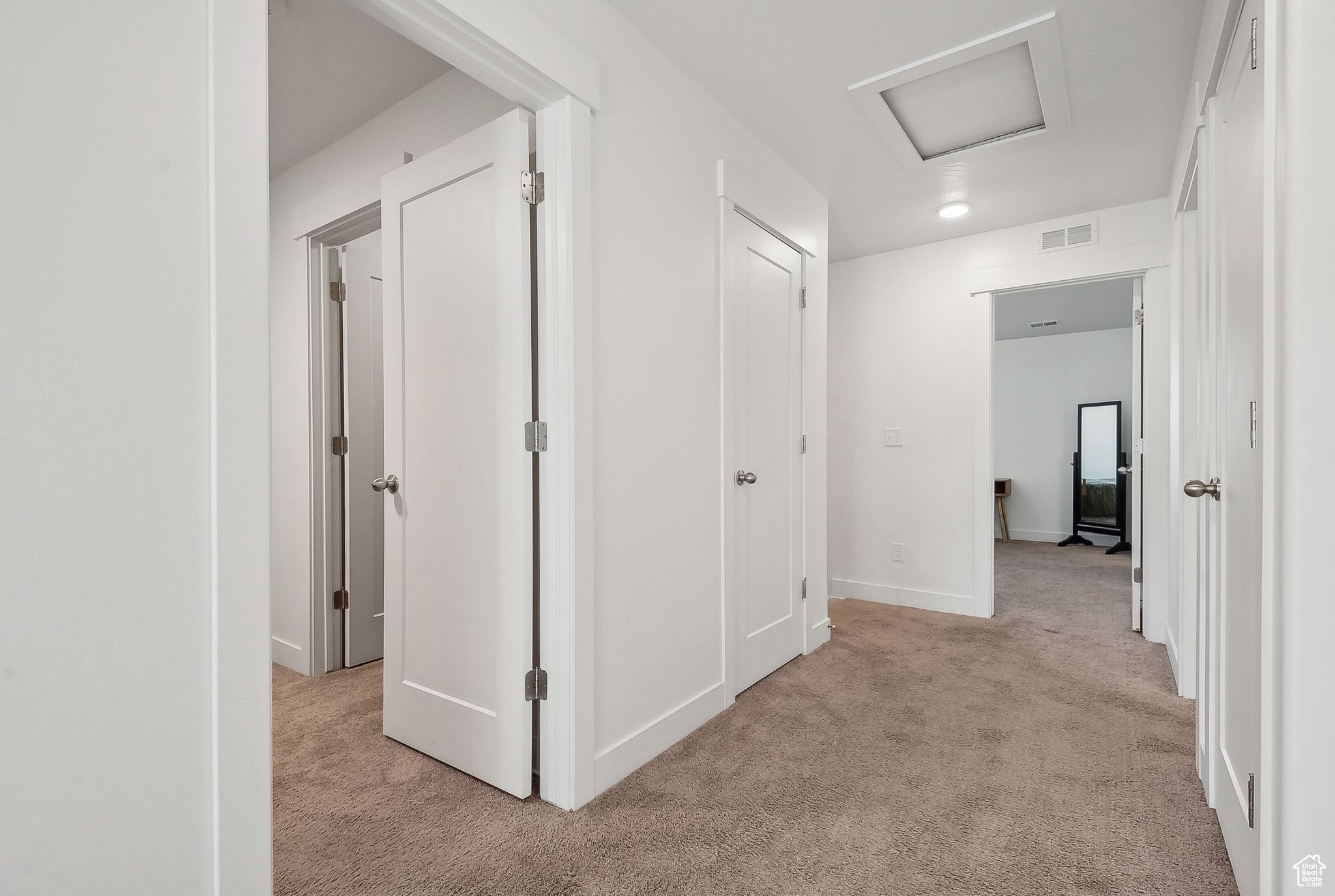 Hallway with light carpet, attic access, visible vents, and baseboards