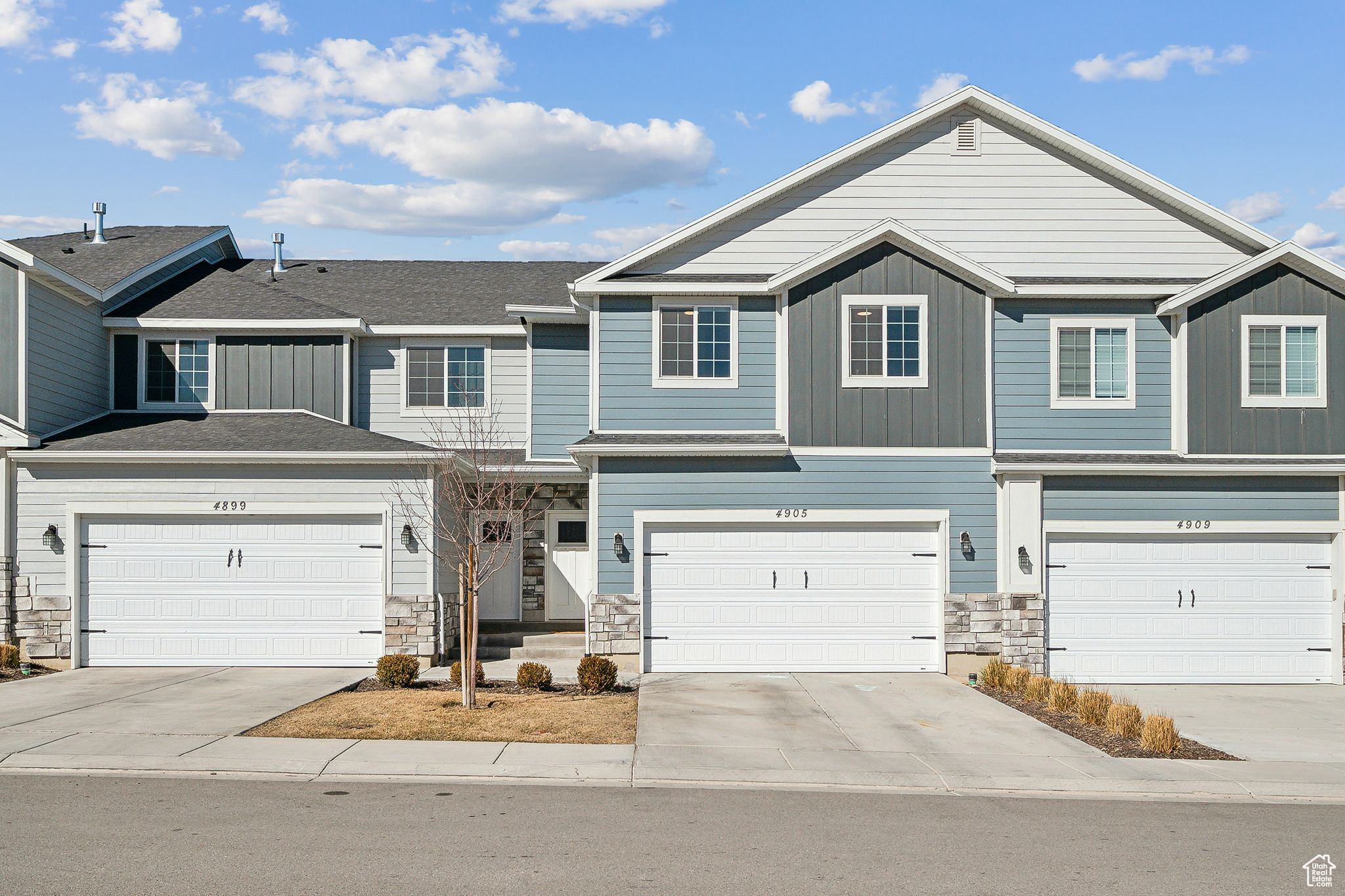 Townhome / multi-family property with driveway, board and batten siding, and stone siding