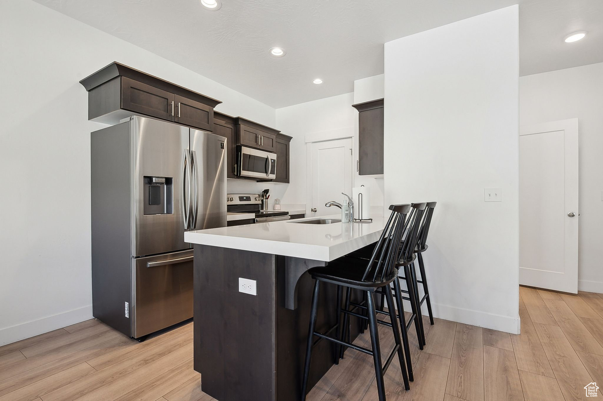 Kitchen with a breakfast bar, appliances with stainless steel finishes, light wood-style floors, a sink, and dark brown cabinetry