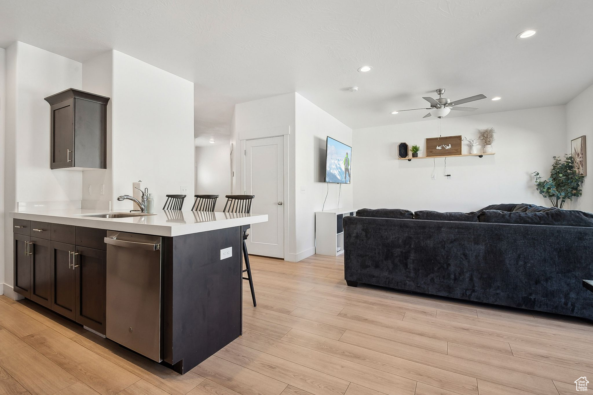 Kitchen with light wood-style flooring, open floor plan, a sink, light countertops, and stainless steel dishwasher
