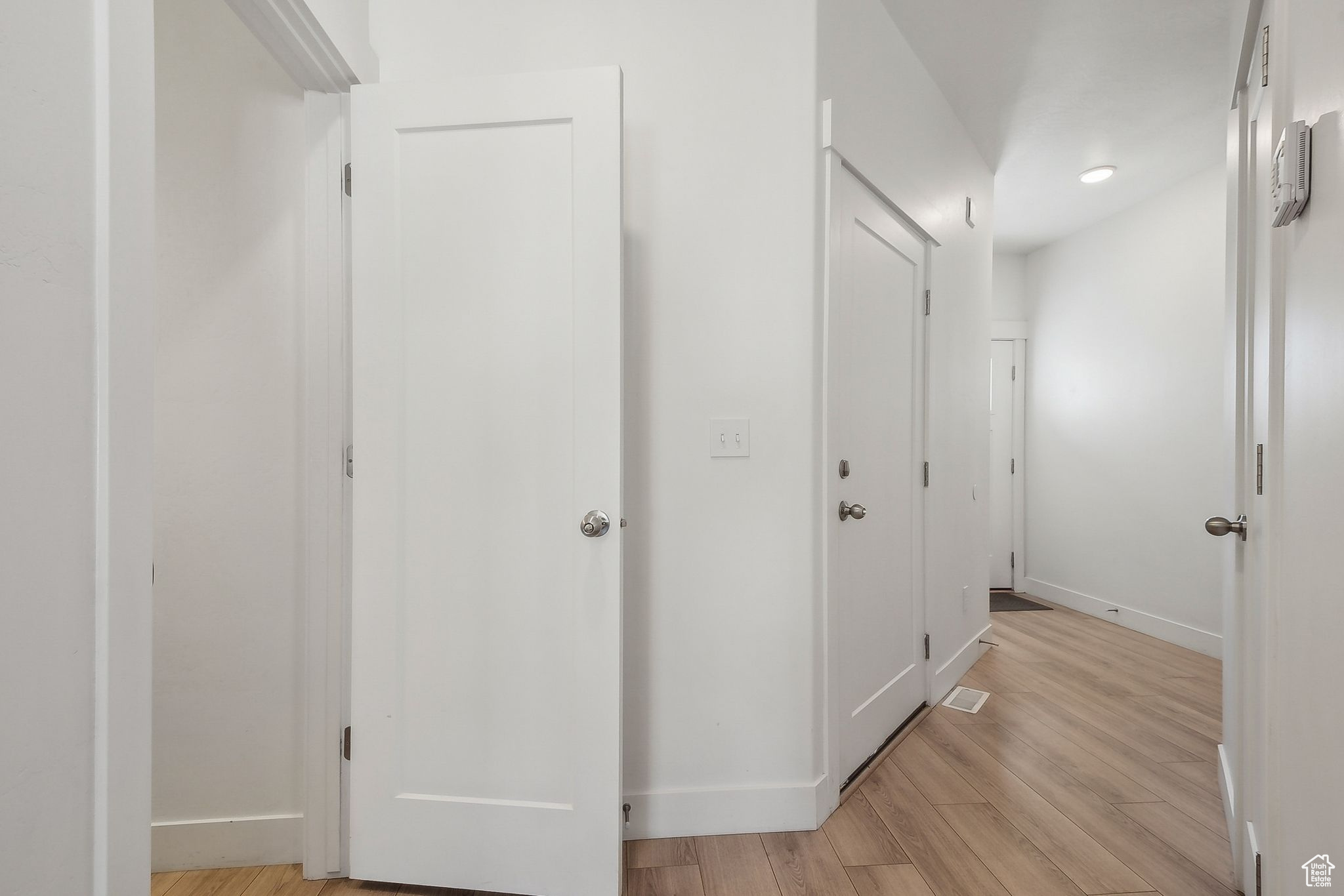 Hallway with light wood-type flooring, visible vents, and baseboards