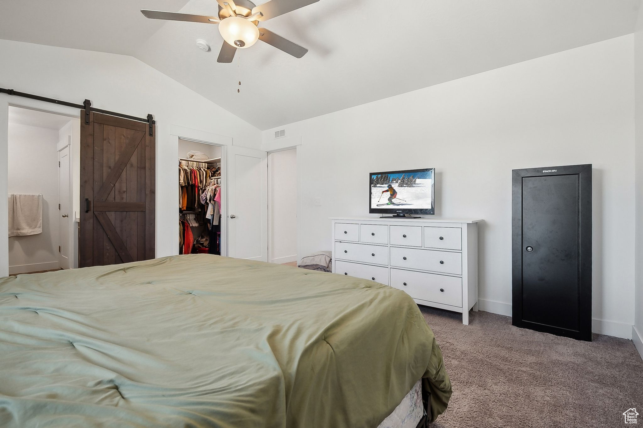 Carpeted bedroom with a barn door, visible vents, a ceiling fan, lofted ceiling, and a spacious closet