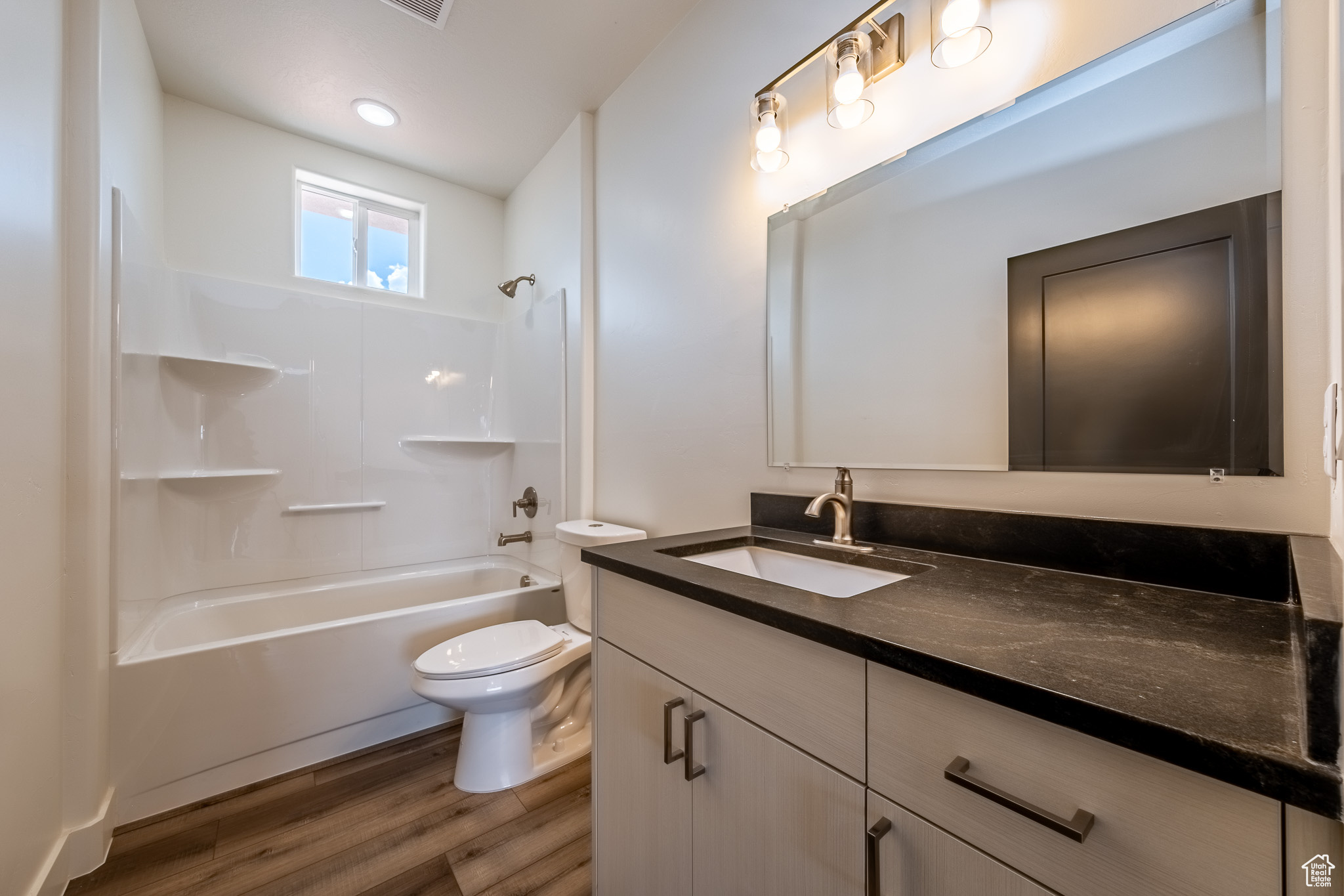 Bathroom featuring vanity, washtub / shower combination, toilet, and wood finished floors