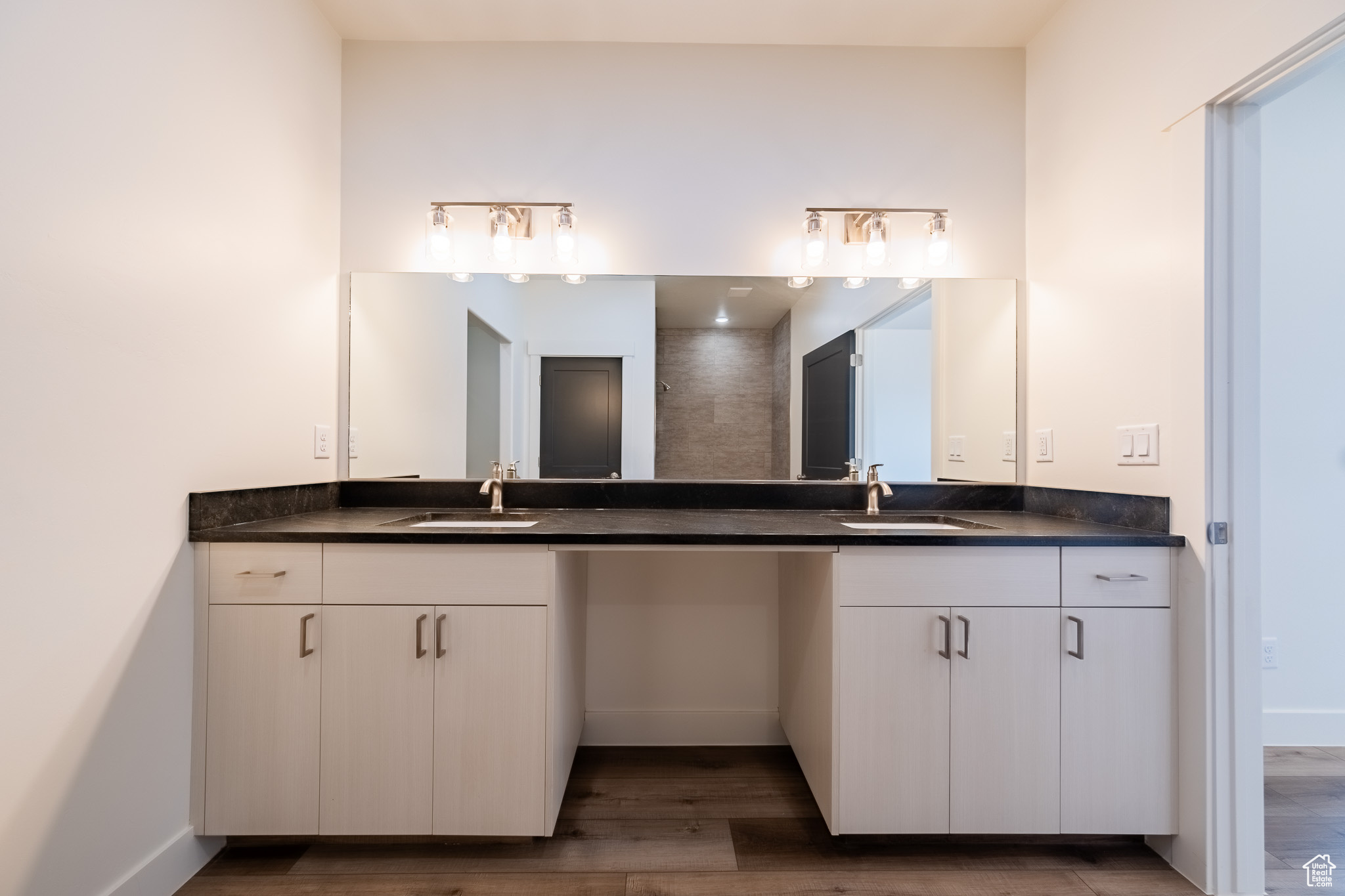 Full bath featuring double vanity, wood finished floors, baseboards, and a sink