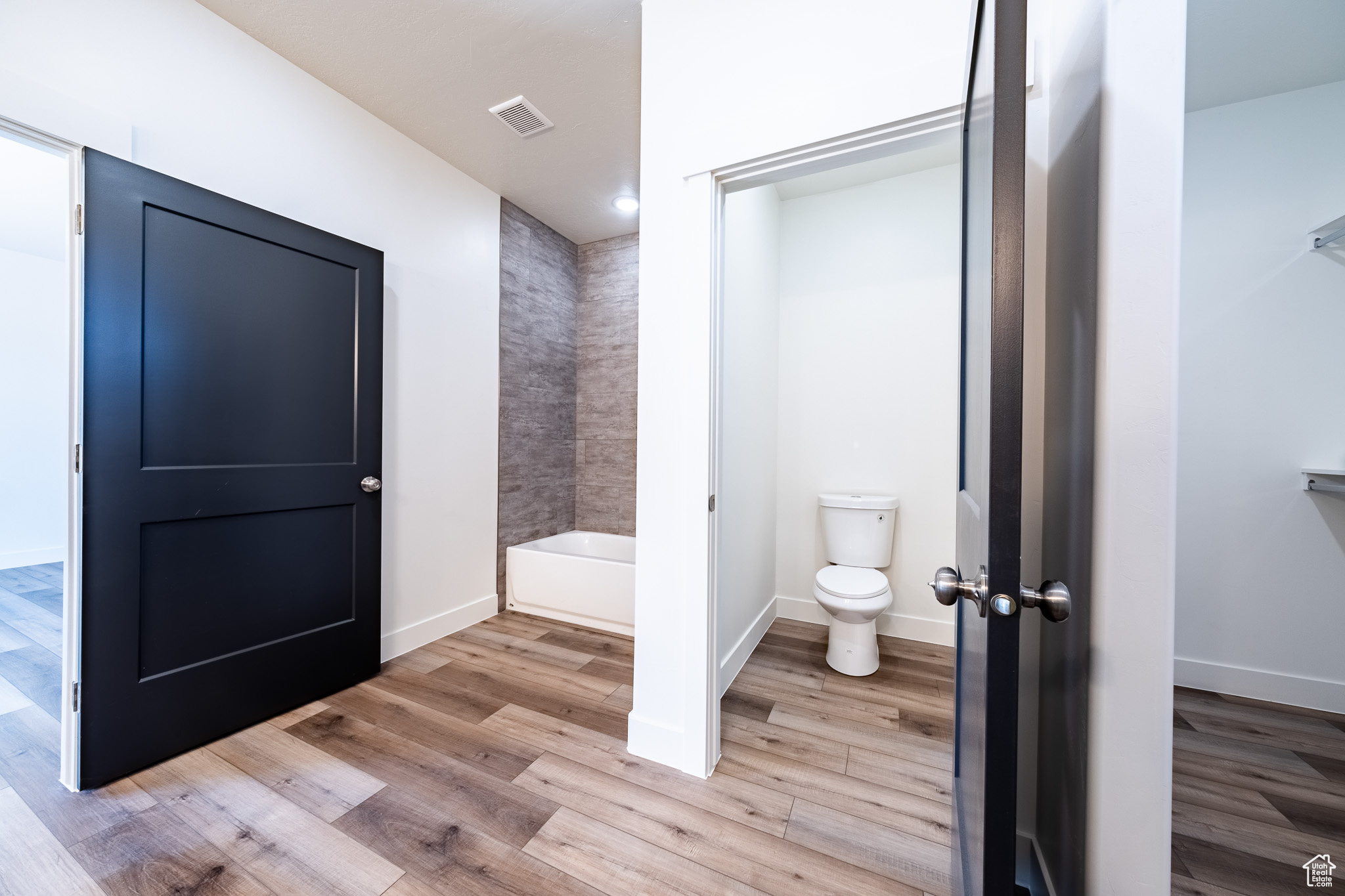 Bathroom featuring wood finished floors, visible vents, baseboards, toilet, and a bath