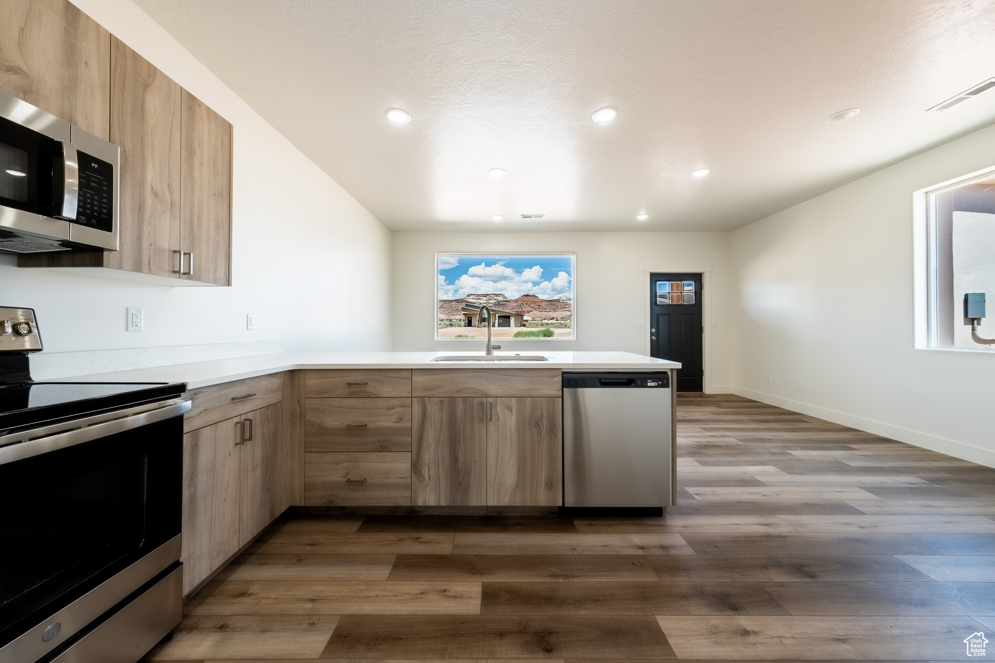 Kitchen featuring modern cabinets, light brown cabinetry, a sink, stainless steel appliances, and a peninsula