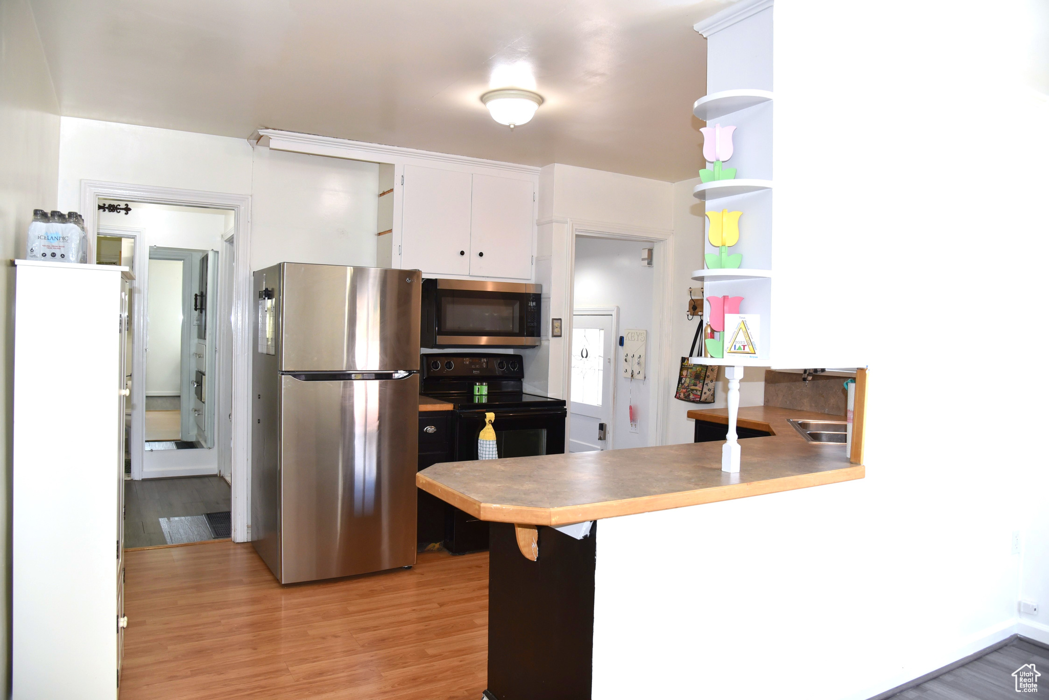 Kitchen with open shelves, light wood-style flooring, a peninsula, stainless steel appliances, and white cabinets