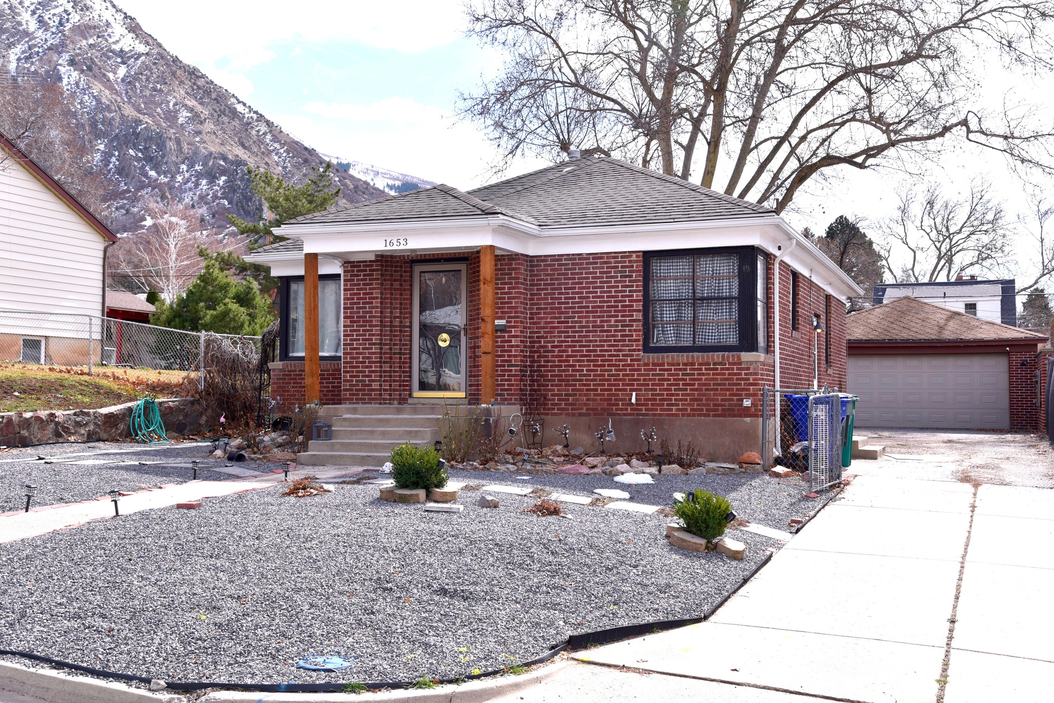 Bungalow-style house featuring fence, an outdoor structure, a shingled roof, a garage, and brick siding