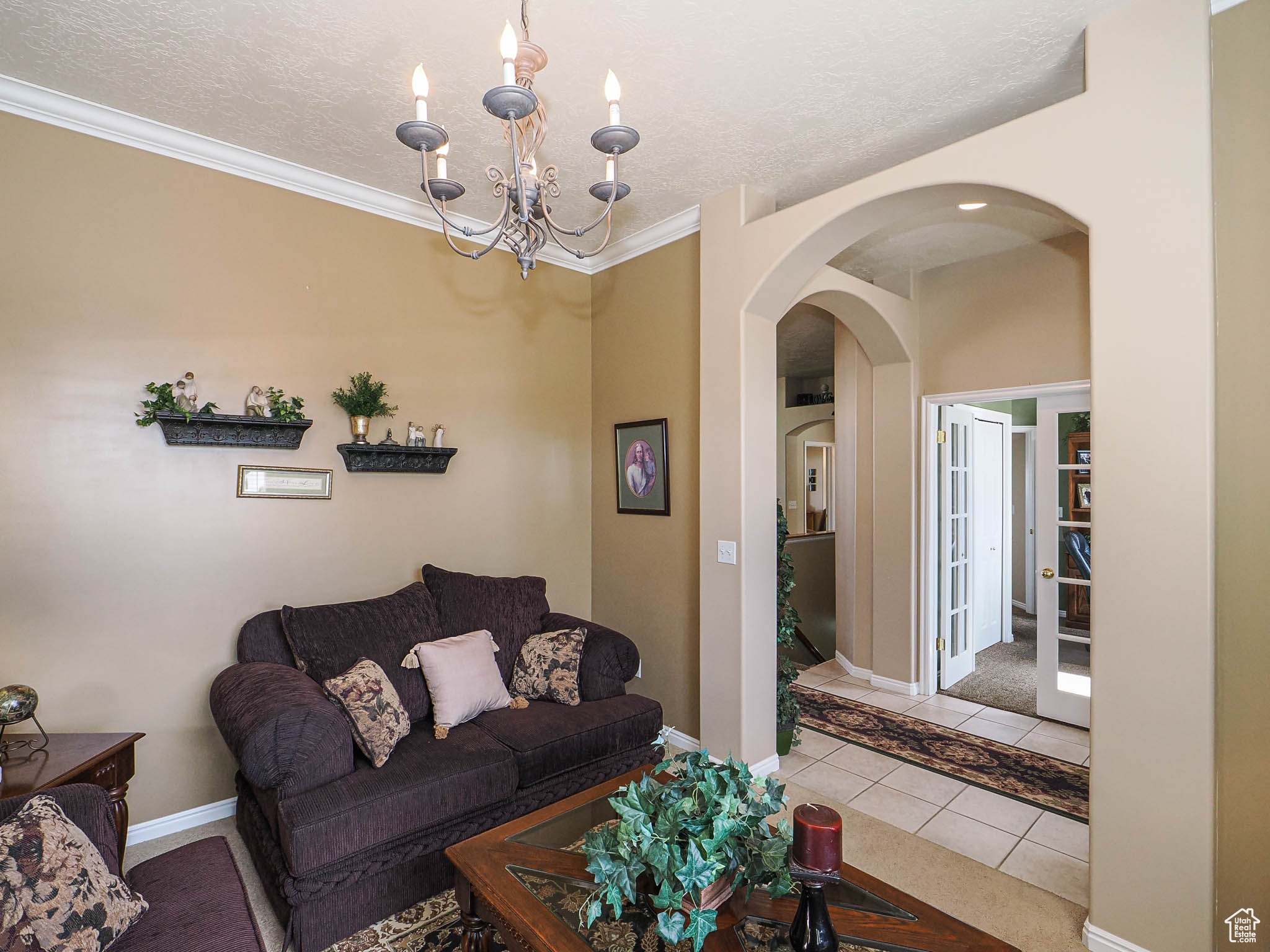 Tiled living area featuring a notable chandelier, ornamental molding, a textured ceiling, arched walkways, and baseboards