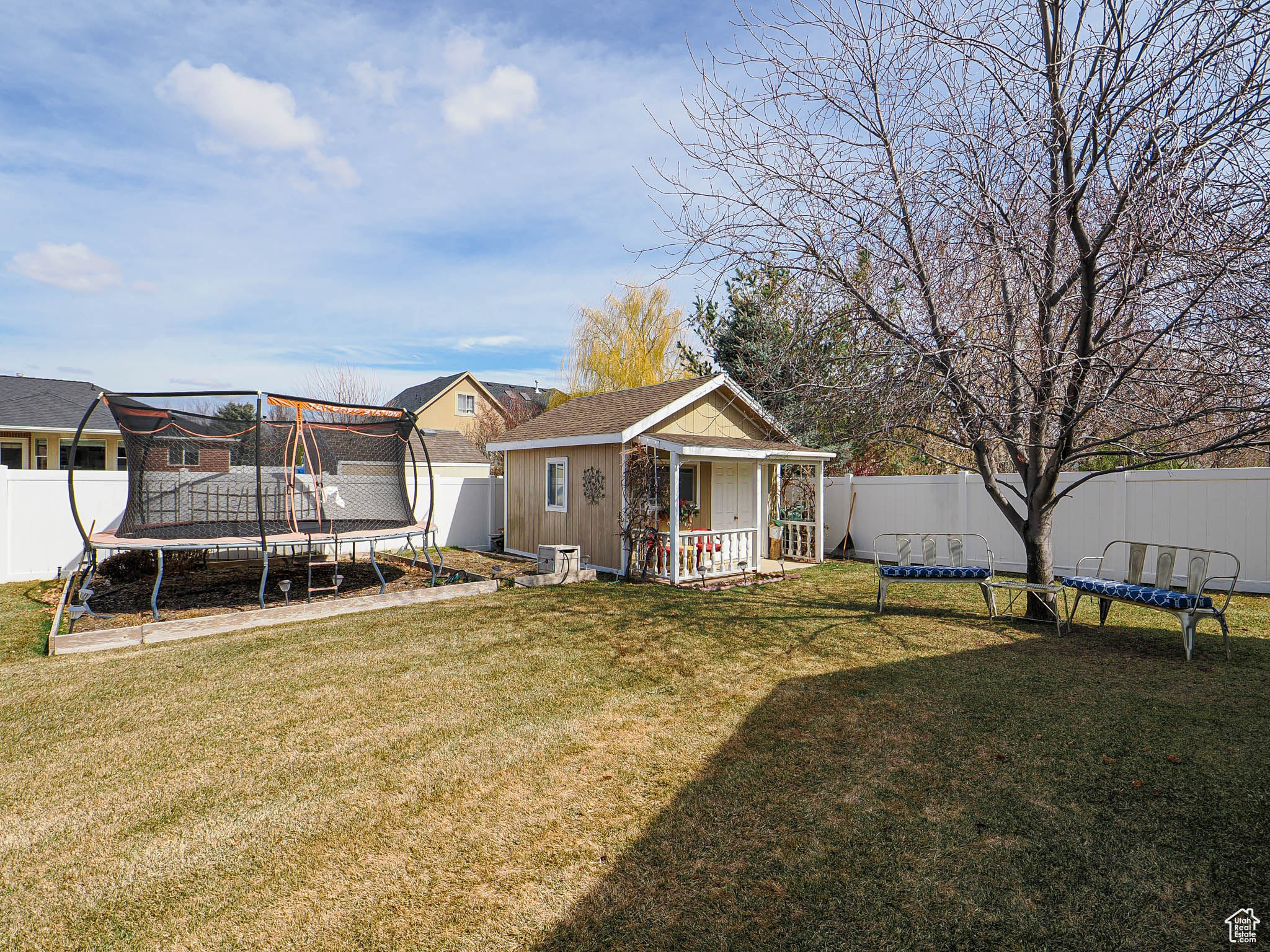 Back of house with an outdoor structure, a trampoline, a fenced backyard, and a lawn