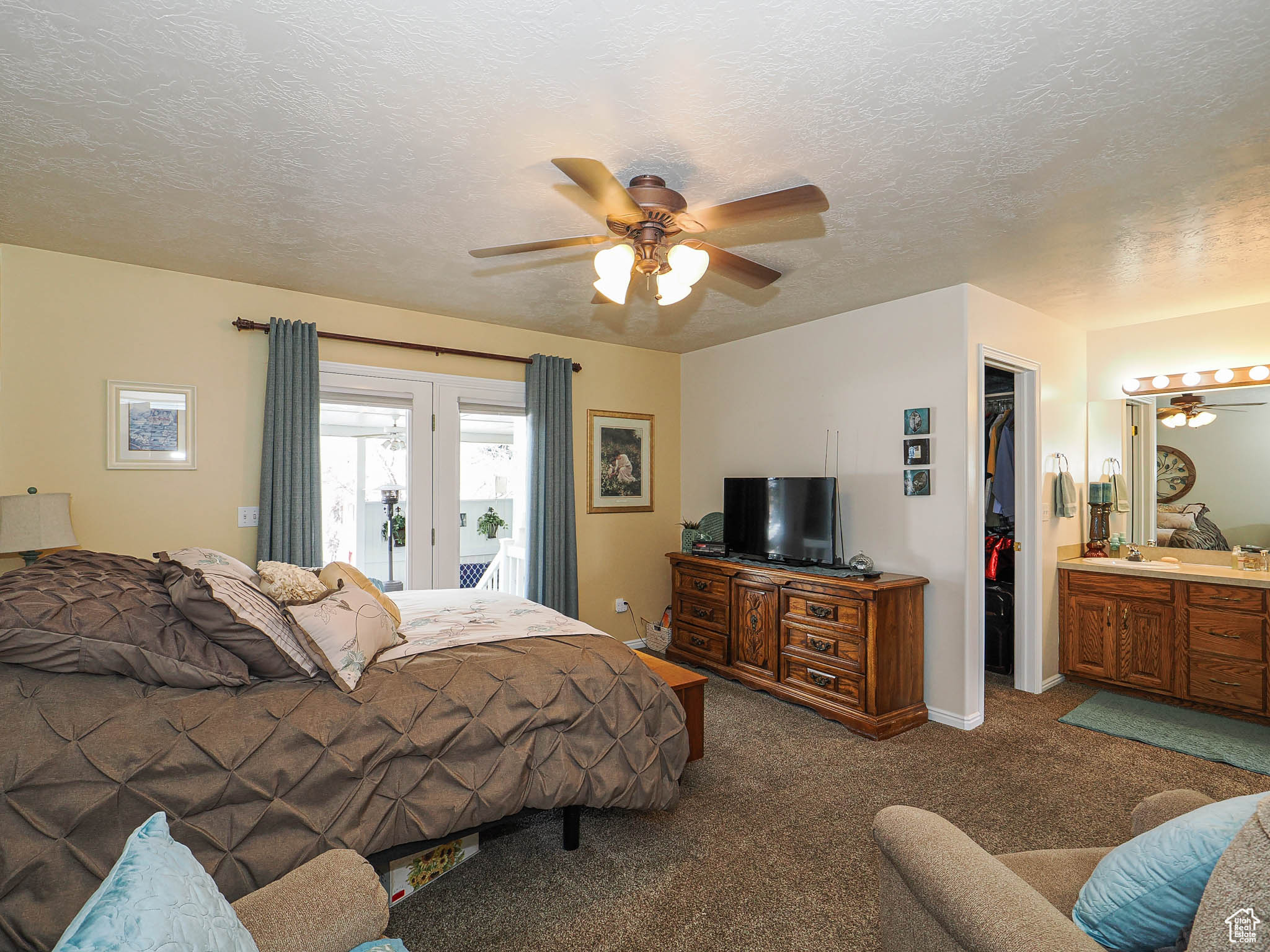 Carpeted bedroom with a ceiling fan, access to outside, a textured ceiling, a closet, and a spacious closet