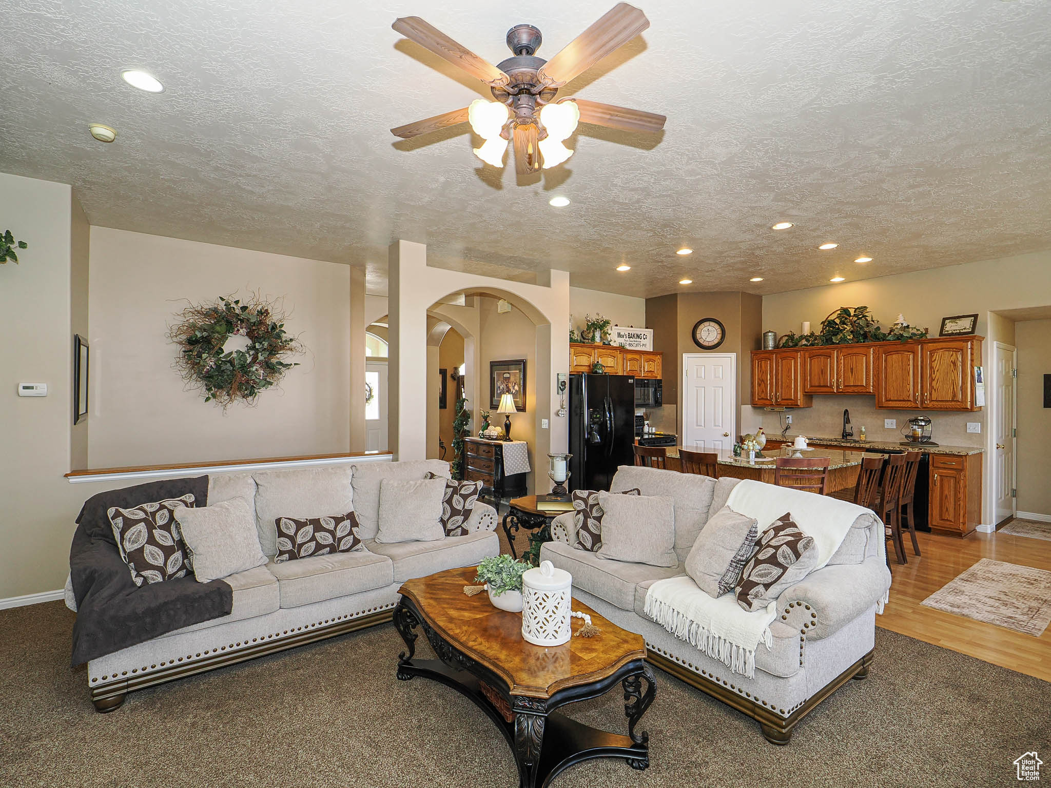 Living room with a textured ceiling, recessed lighting, arched walkways, light wood finished floors, and baseboards
