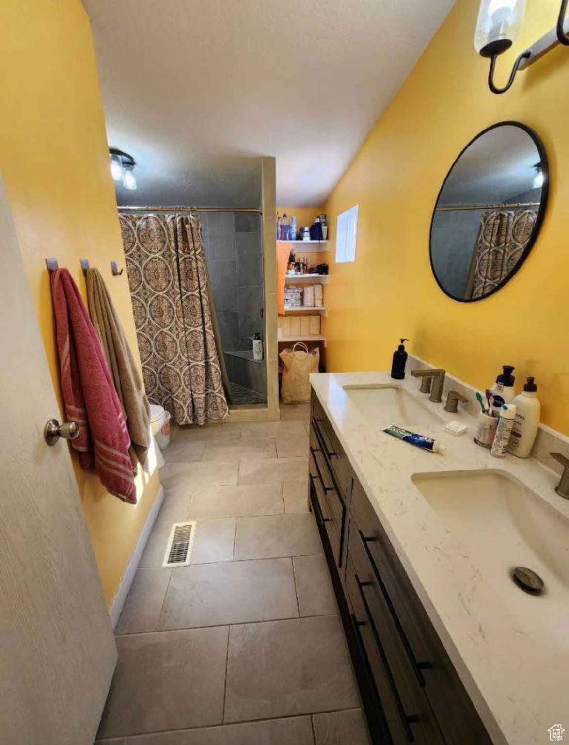 Bathroom with double vanity, tiled shower, visible vents, and a sink