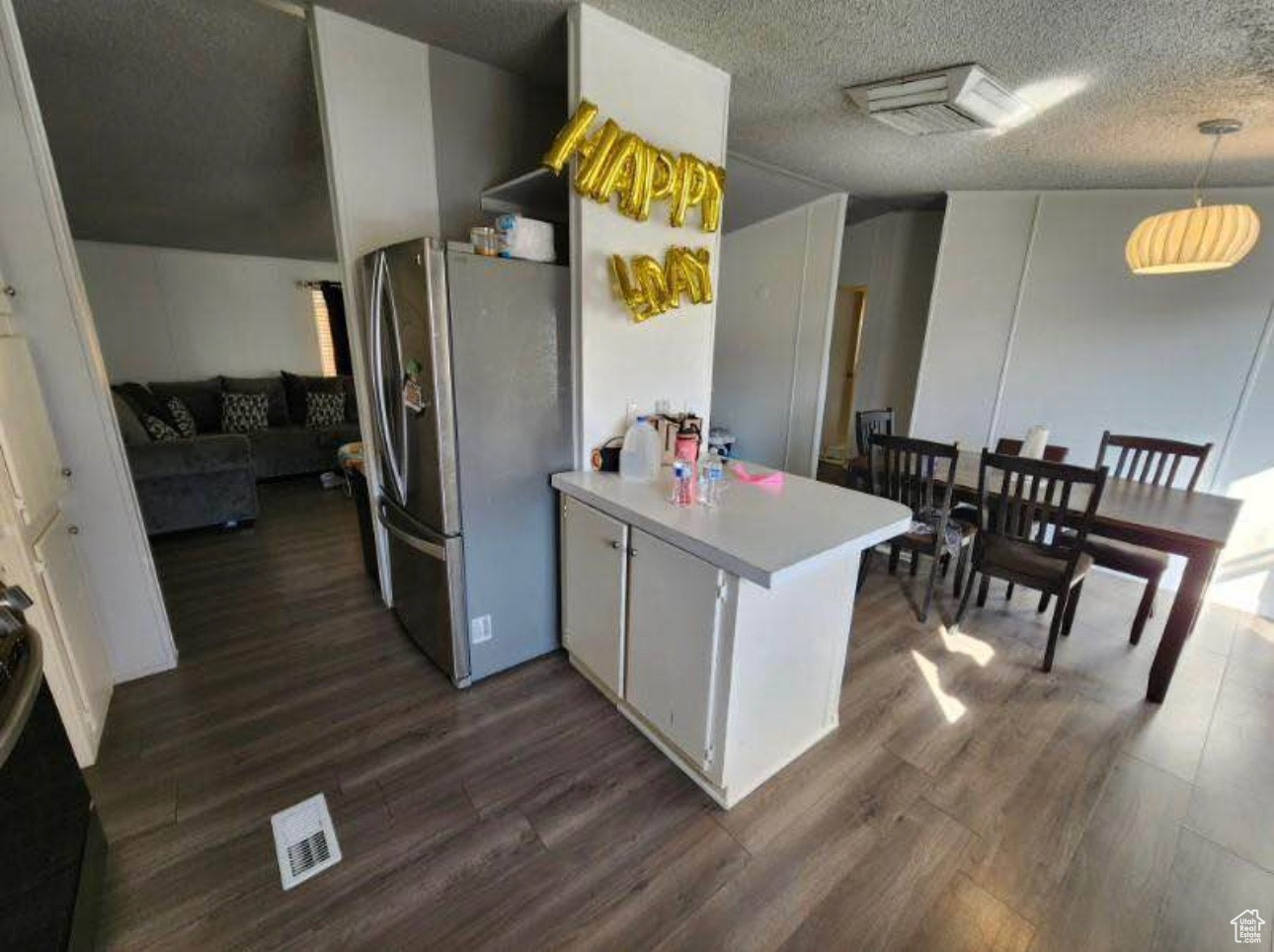 Kitchen with visible vents, a textured ceiling, dark wood-style floors, freestanding refrigerator, and a peninsula