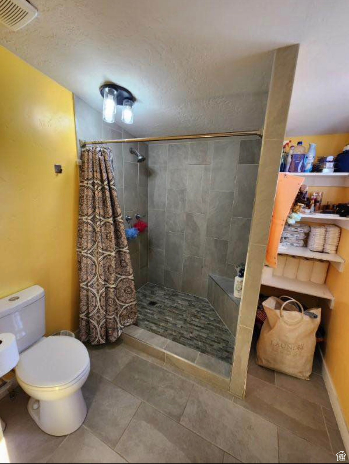 Bathroom featuring toilet, visible vents, a tile shower, and a textured ceiling