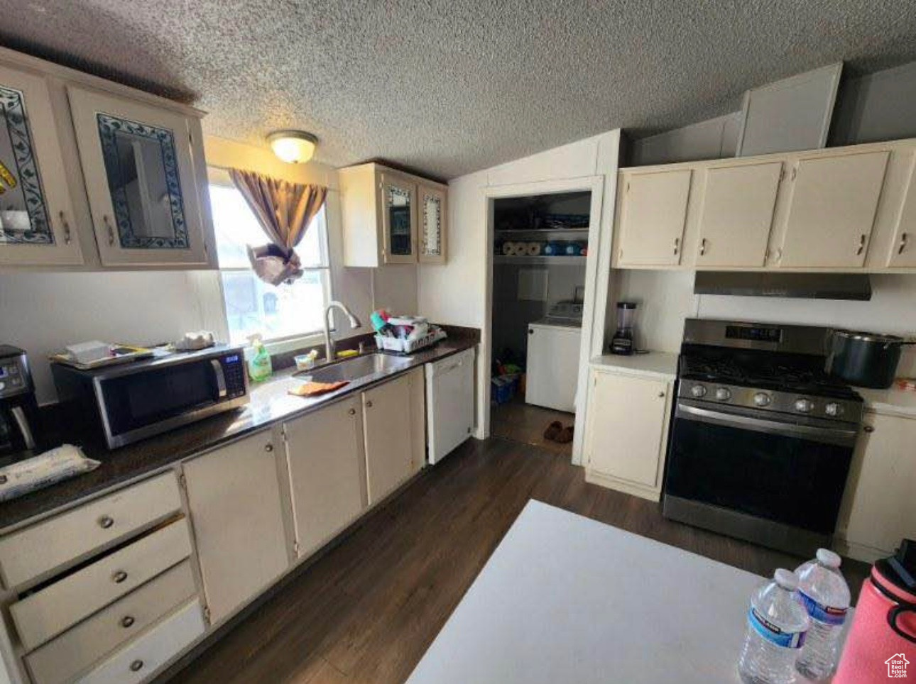 Kitchen featuring a sink, under cabinet range hood, washer / clothes dryer, dark wood finished floors, and stainless steel appliances