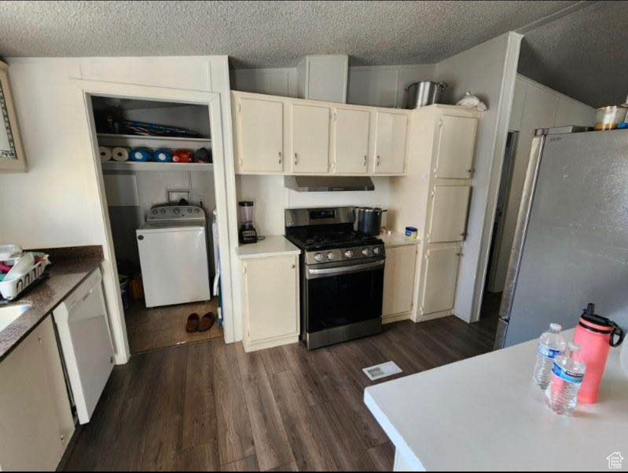 Kitchen with dark wood finished floors, a textured ceiling, washer / clothes dryer, and stainless steel appliances