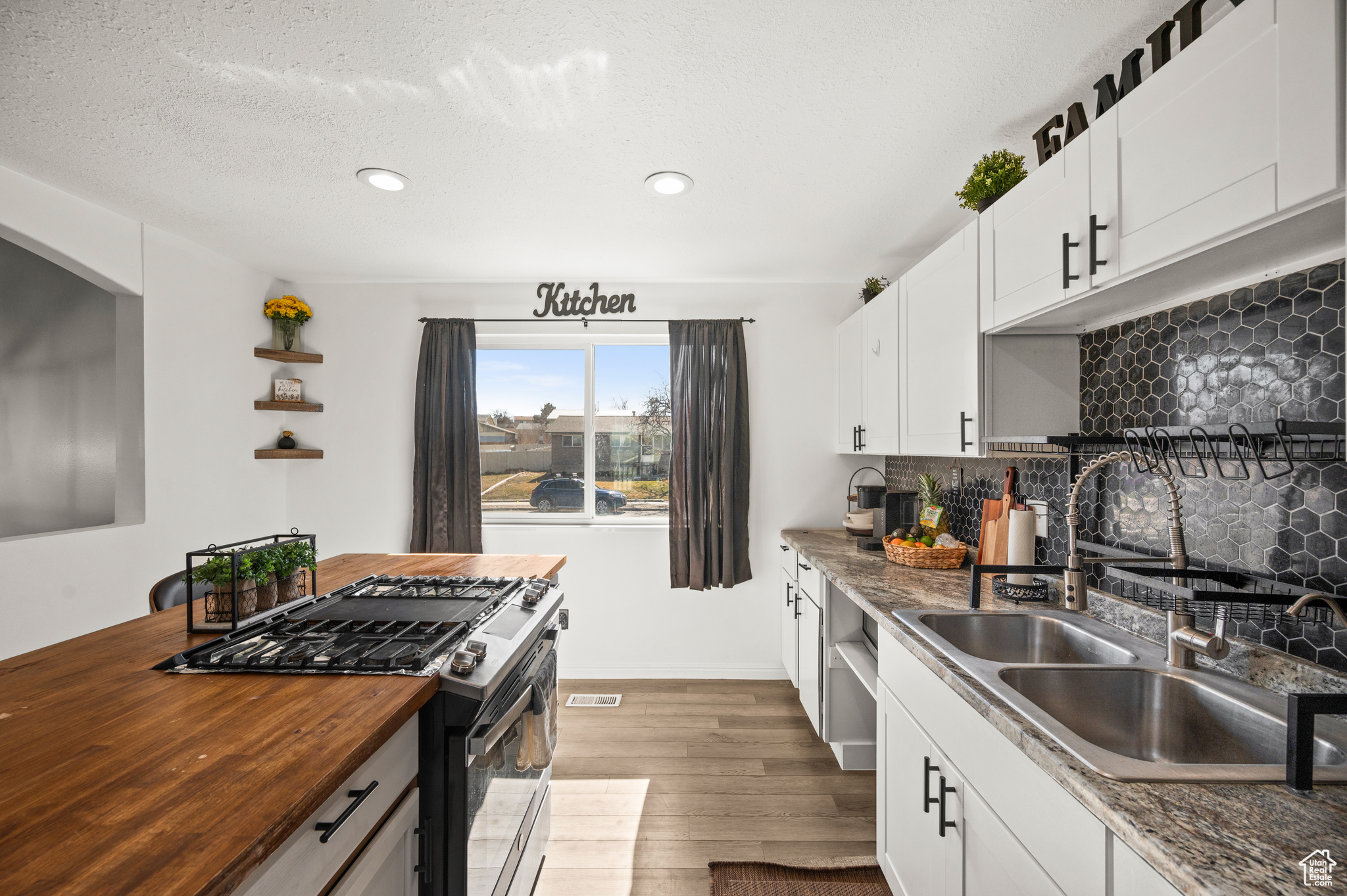 Kitchen with butcher block countertops, decorative backsplash, wood finished floors, gas stove, and a sink