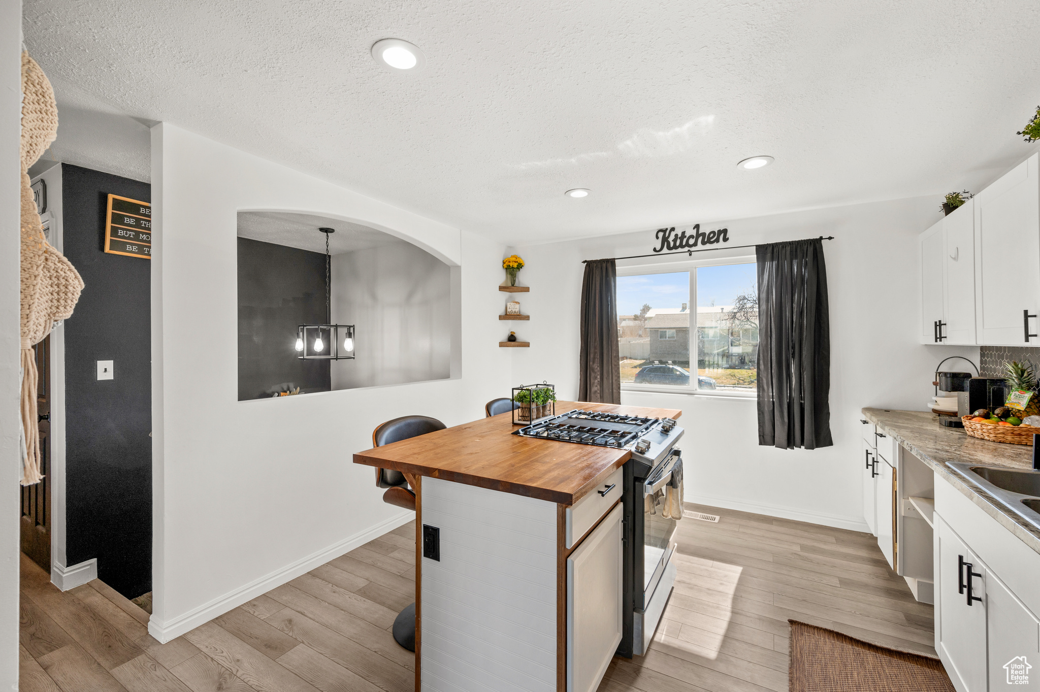 Kitchen featuring a breakfast bar area, gas range oven, light wood-style flooring, white cabinetry, and wood counters