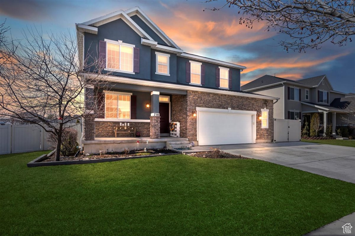 View of front of home with a front yard, fence, stone siding, and driveway