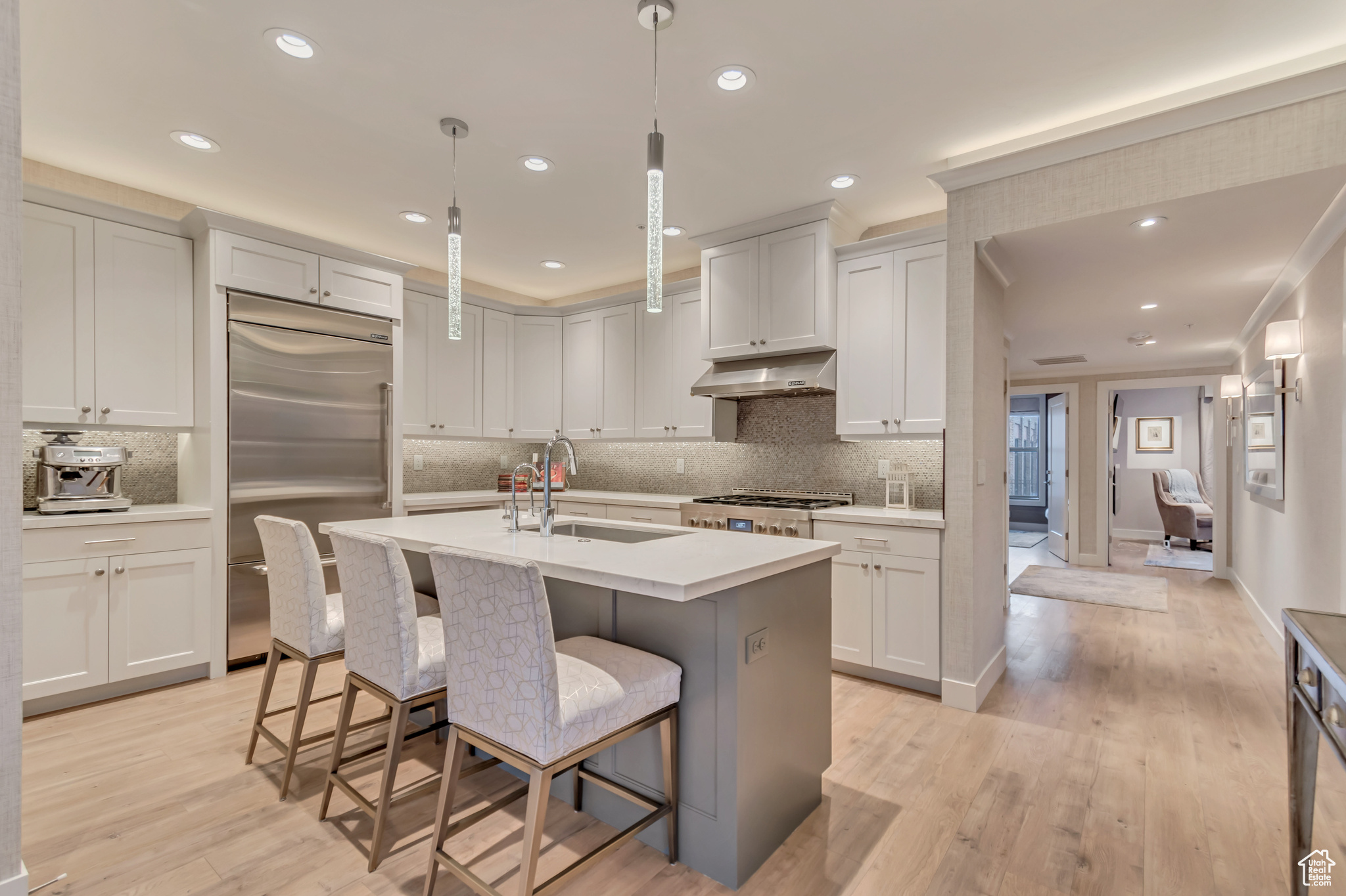 Kitchen featuring a sink, light countertops, under cabinet range hood, range, and stainless steel built in refrigerator