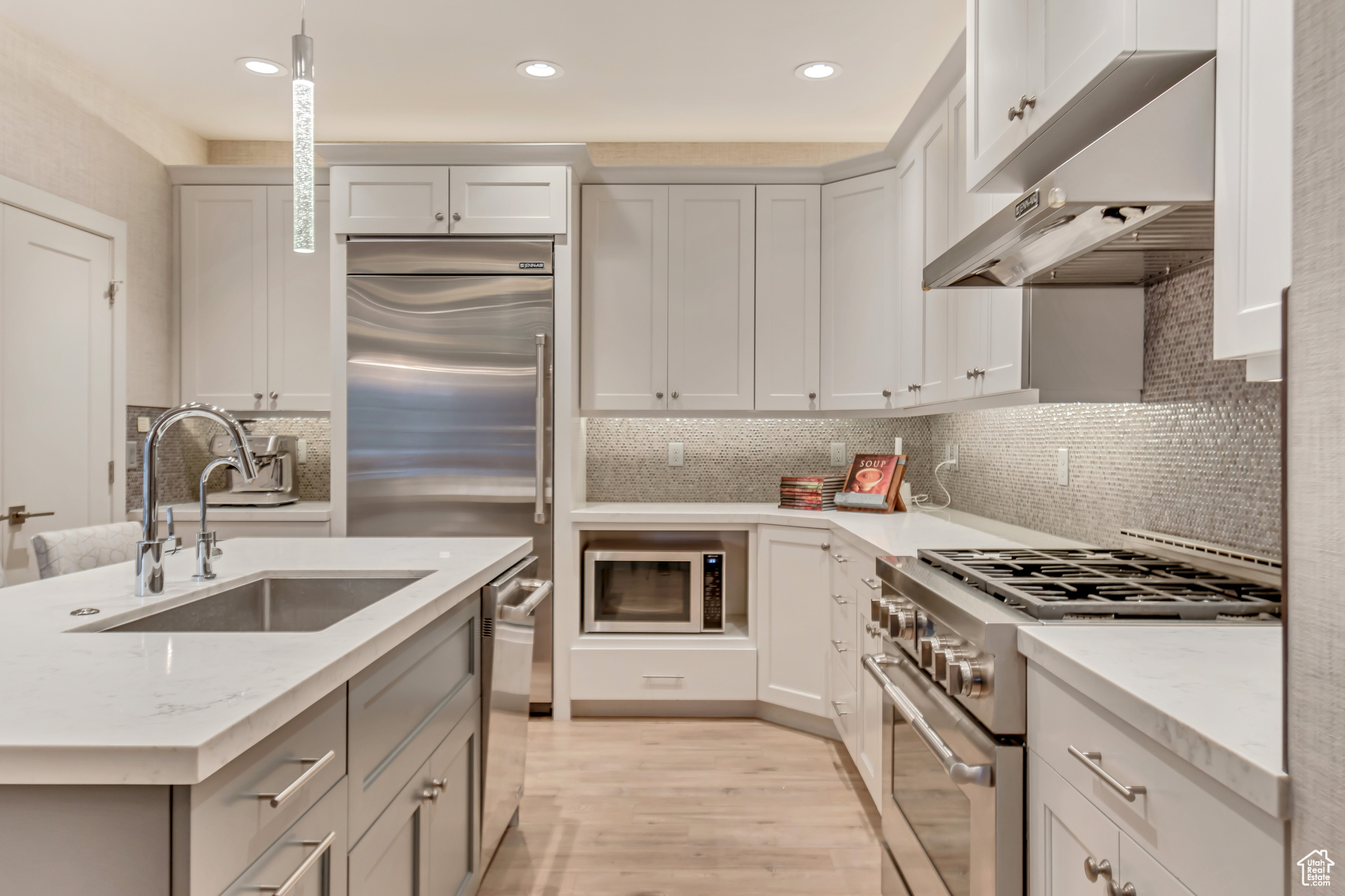 Kitchen with light wood-style flooring, a sink, under cabinet range hood, pendant lighting, and built in appliances