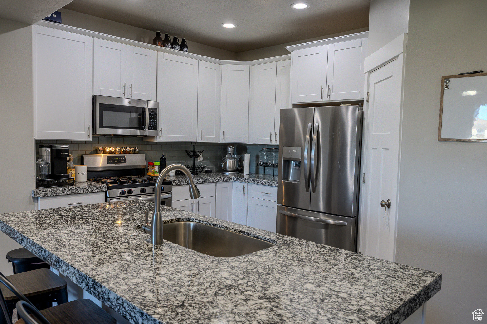 Kitchen with tasteful backsplash, a kitchen bar, appliances with stainless steel finishes, white cabinets, and a sink