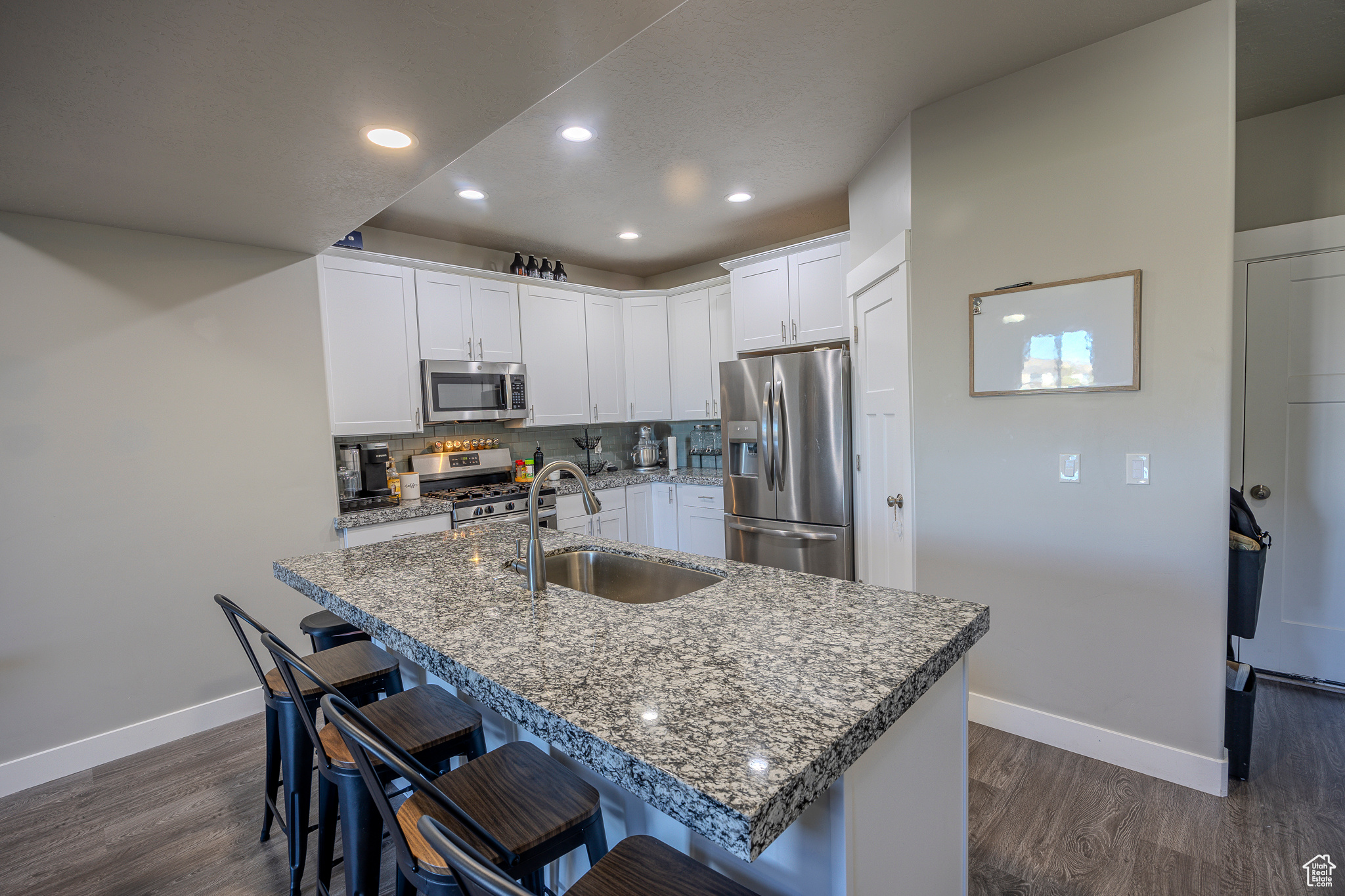 Kitchen with backsplash, dark wood finished floors, a kitchen bar, stainless steel appliances, and a sink