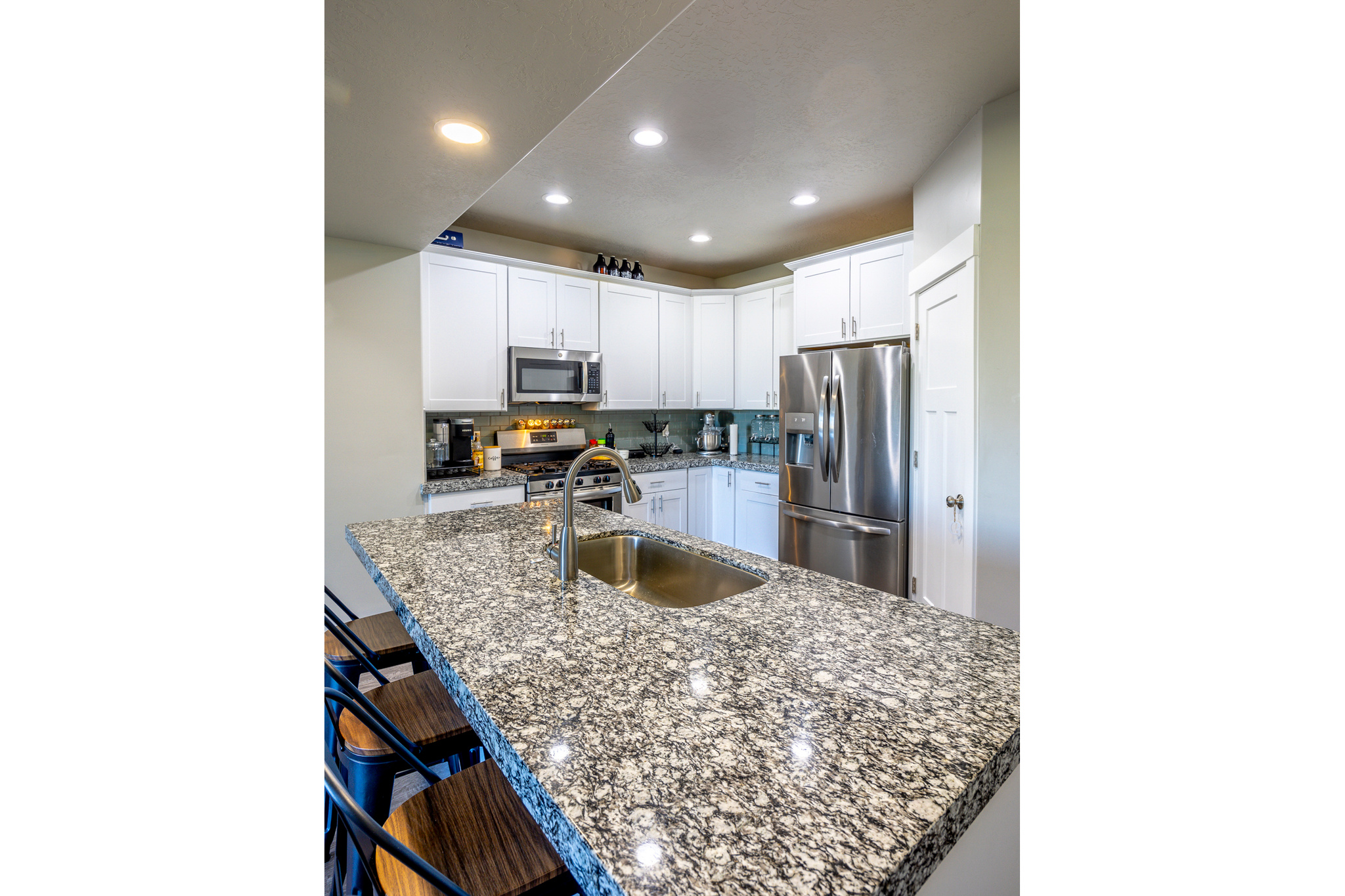 Kitchen with a sink, decorative backsplash, white cabinets, appliances with stainless steel finishes, and a kitchen bar