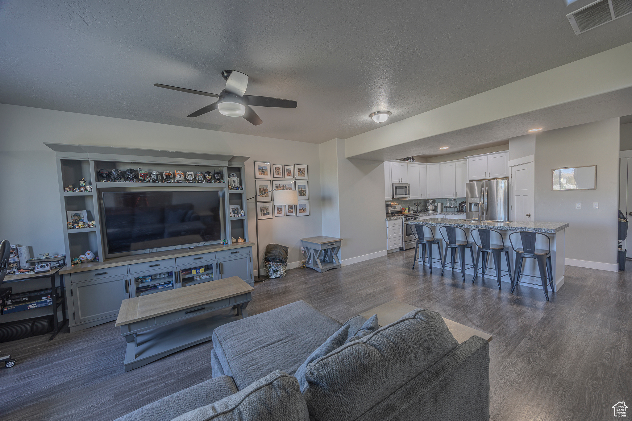 Living area with dark wood-style floors, visible vents, a ceiling fan, and baseboards