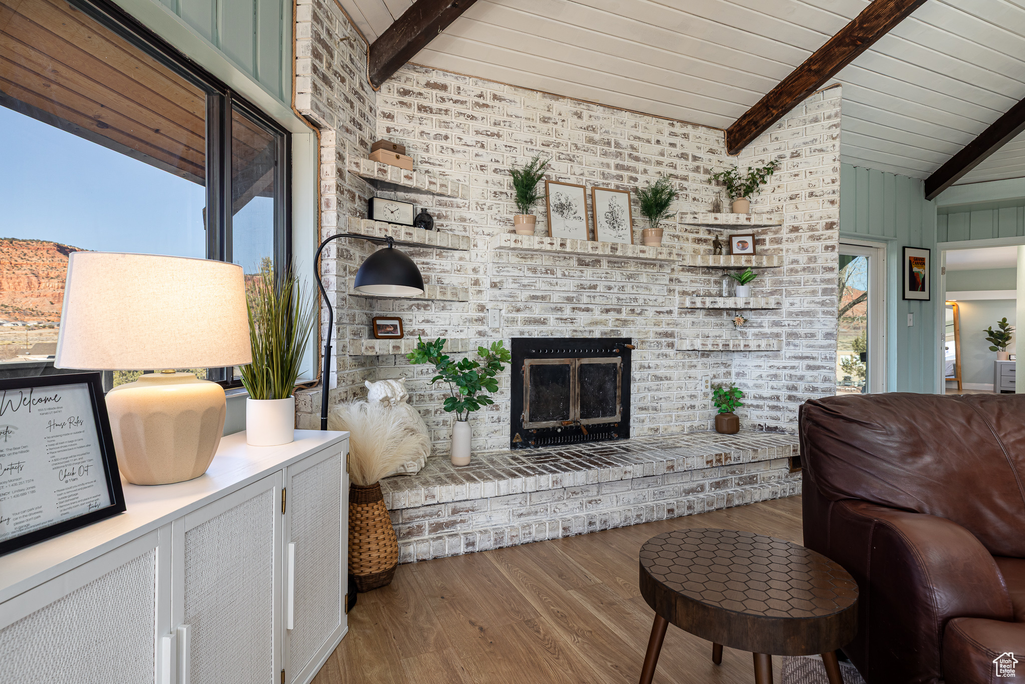 Living room featuring wood finished floors, wooden ceiling, a fireplace, brick wall, and vaulted ceiling with beams