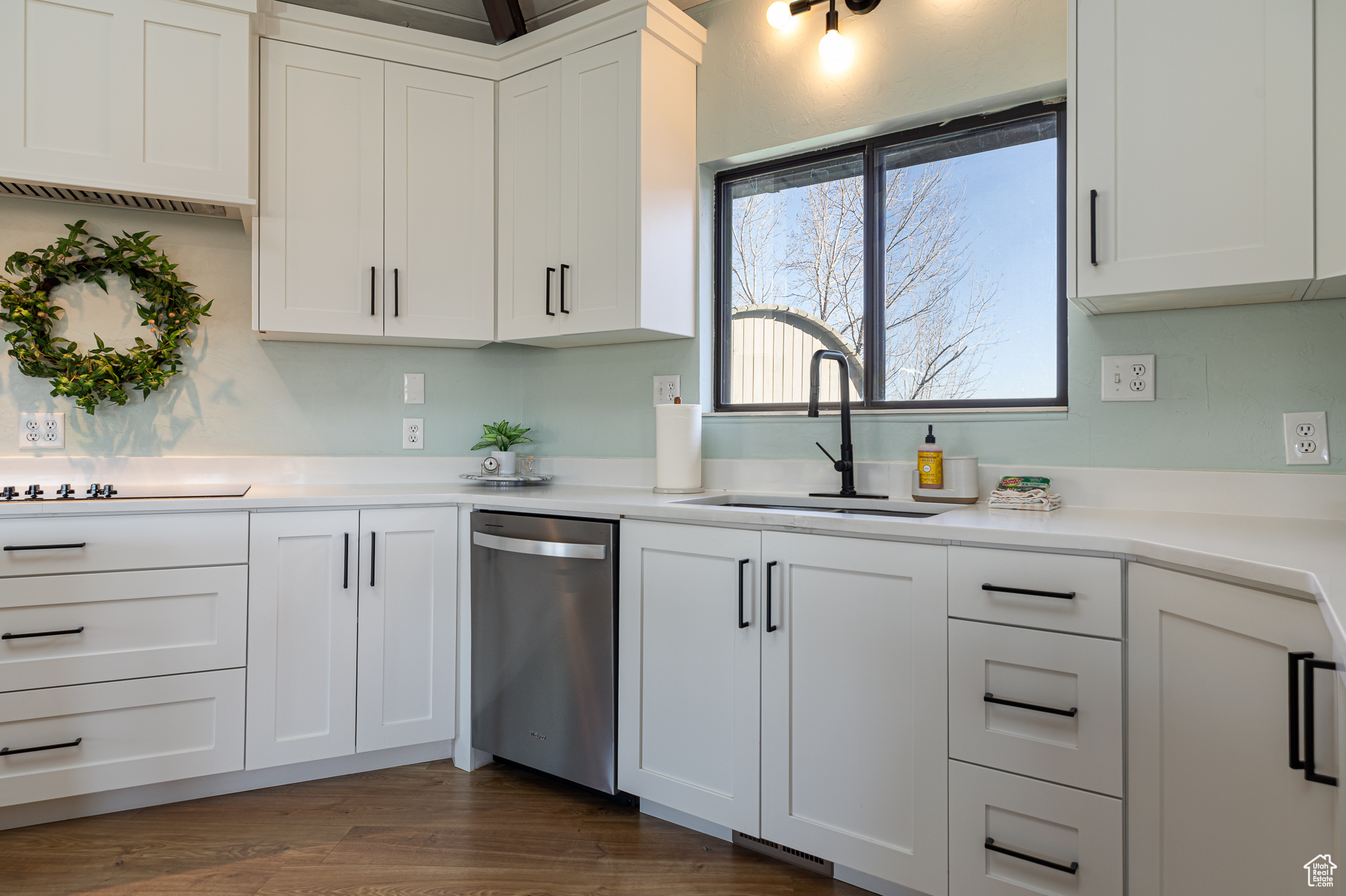 Kitchen featuring a sink, black electric cooktop, stainless steel dishwasher, and white cabinetry