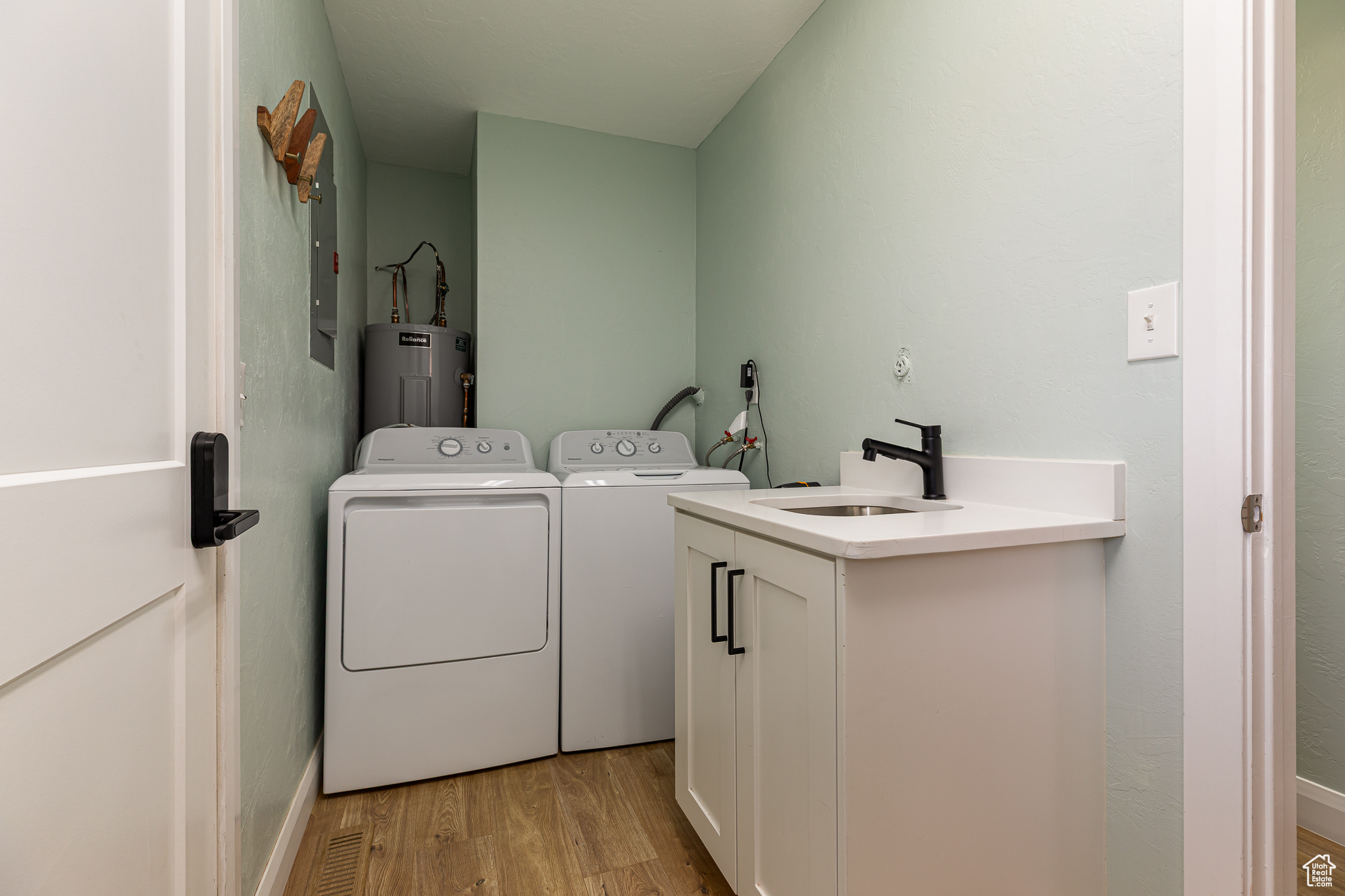 Clothes washing area featuring a sink, water heater, cabinet space, separate washer and dryer, and light wood finished floors