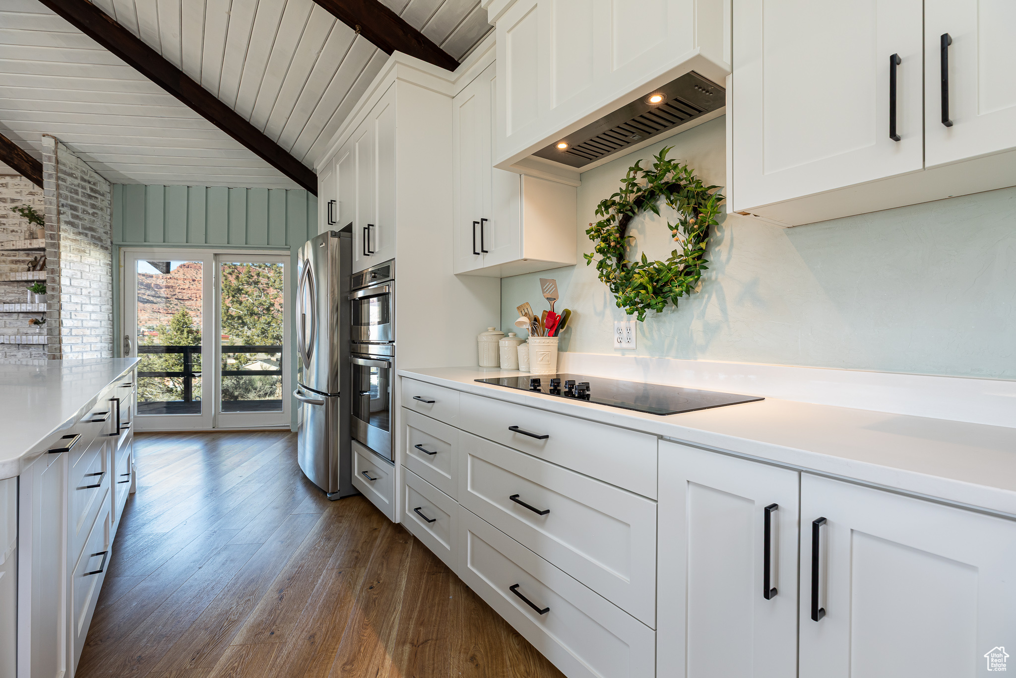 Kitchen featuring beamed ceiling, dark wood-style floors, appliances with stainless steel finishes, light countertops, and custom exhaust hood