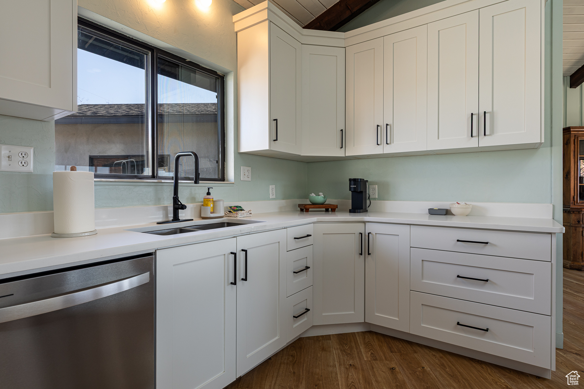 Kitchen with a sink, dark wood-type flooring, white cabinets, light countertops, and dishwasher