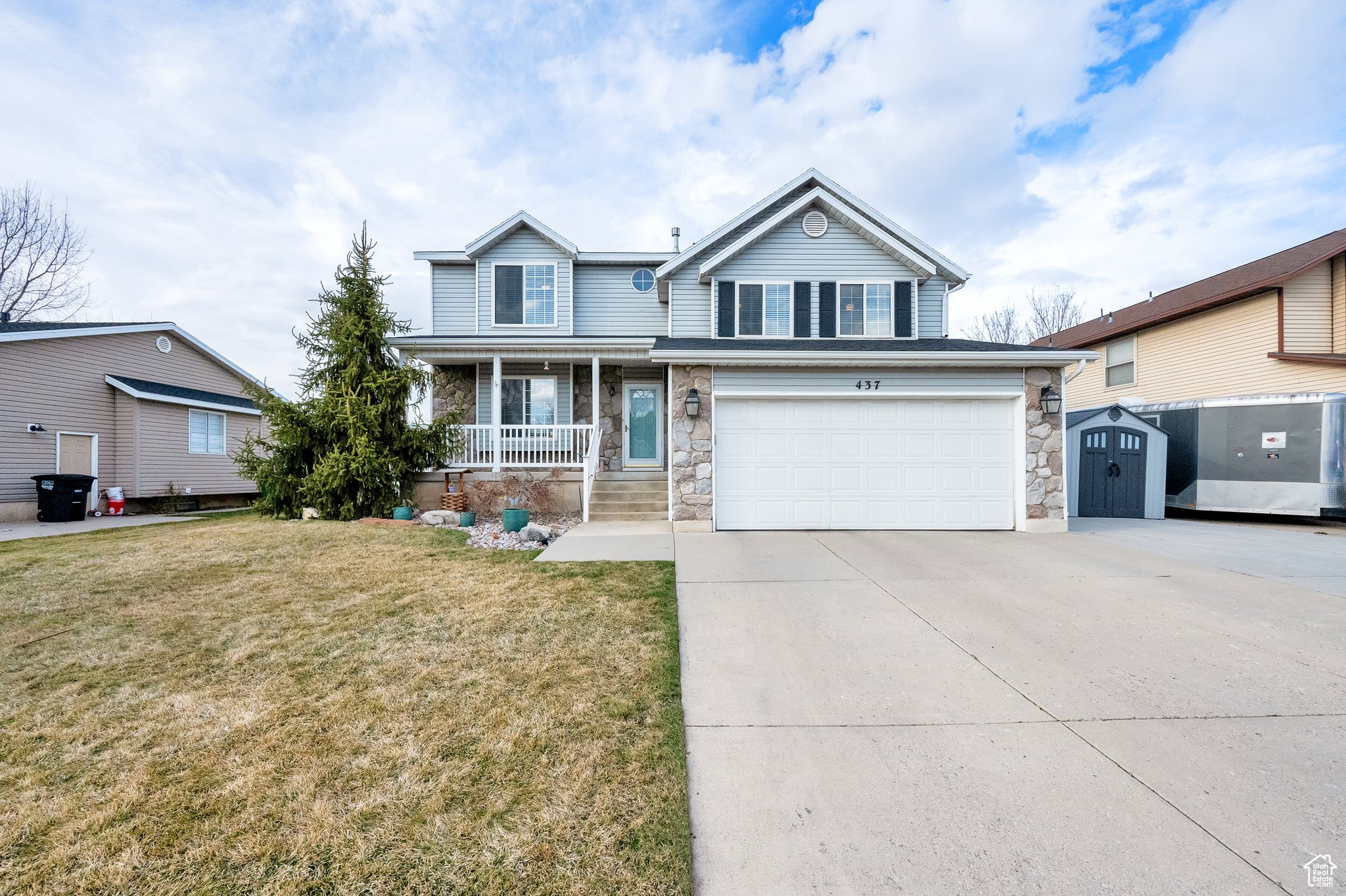 Traditional home featuring a porch, concrete driveway, stone siding, and a front yard