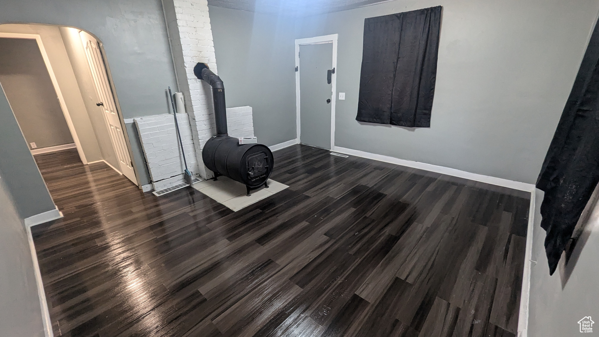 Interior space featuring arched walkways, a wood stove, baseboards, and wood finished floors